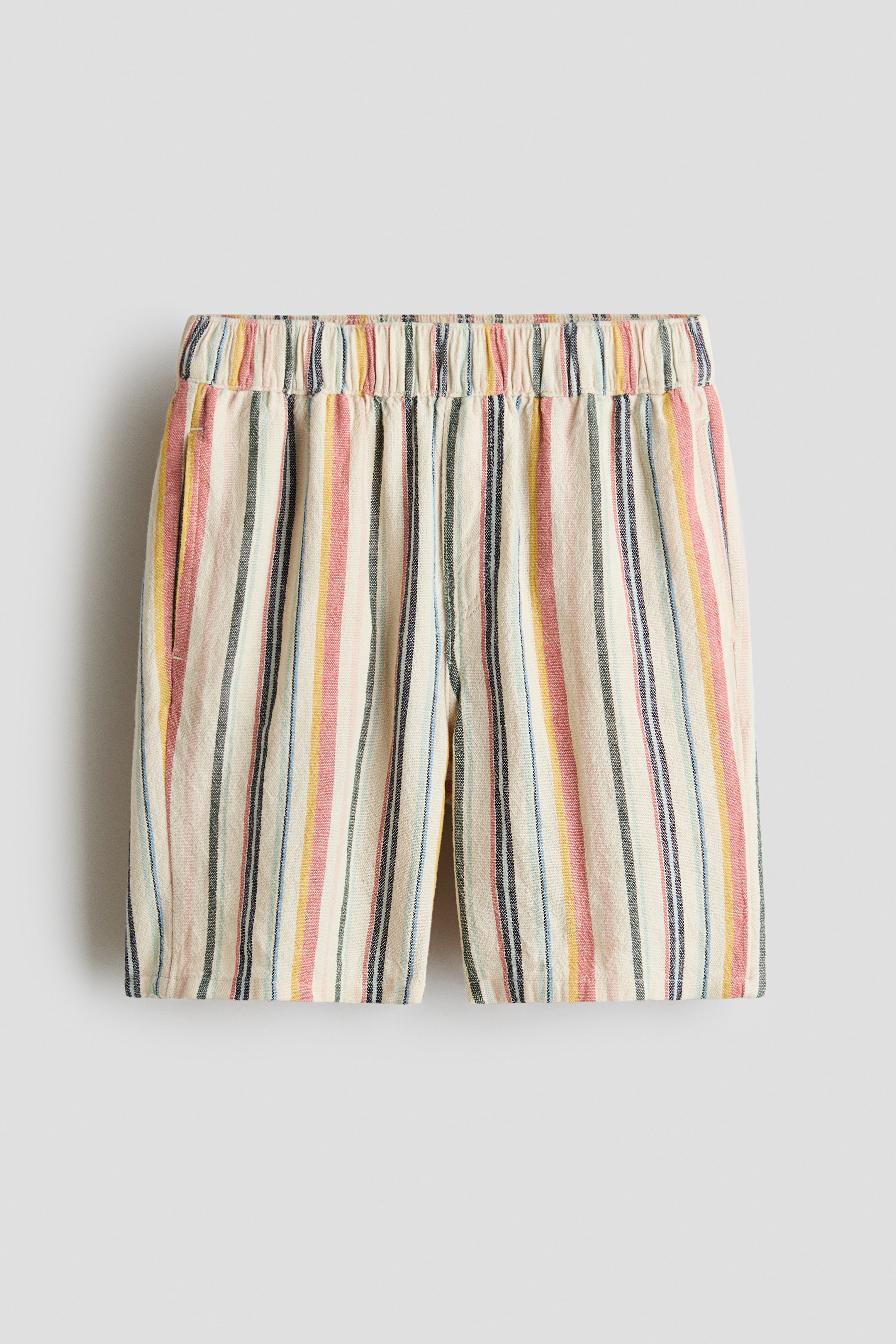 View larger image: The shorts are facing front, with an elasticated, gathered waistband. They display a multicoloured vertical stripe pattern in shades of red, pink, yellow, blue, black and green on a cream background, with side-seam pockets visible.