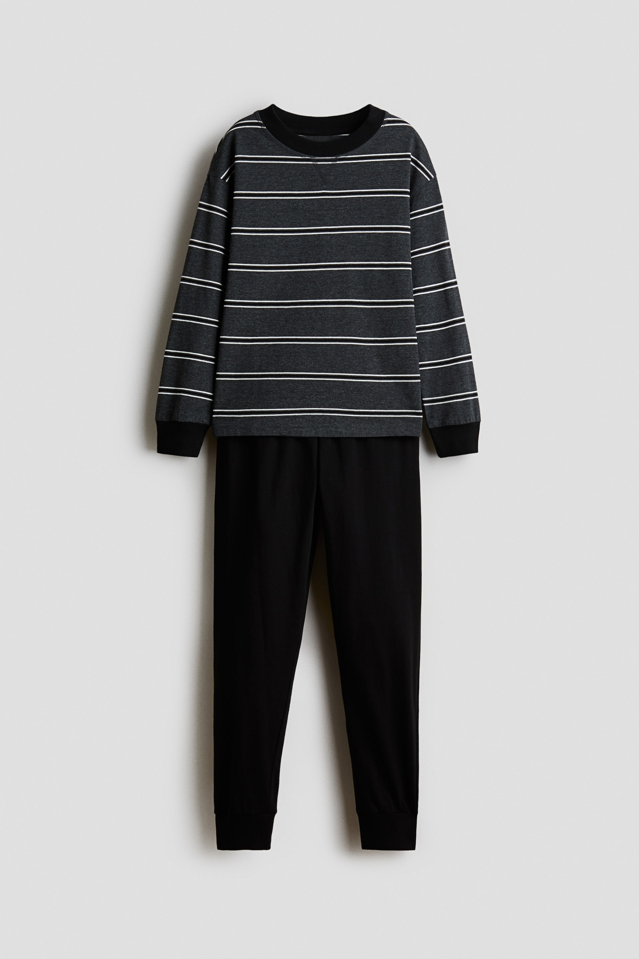 Größeres Bild ansehen: Eine frontale Ansicht eines Pyjama-Sets mit einem dunkelgrauen Langarmoberteil mit horizontalen weißen Streifen und einer dazu passenden einfarbig schwarzen Hose. Das Oberteil verfügt über einen gerippten Rundhalsausschnitt mit kleinem V-Nahtdetail, überschnittene Schultern und schwarze gerippte Bündchen, während die Hose eine zulaufende Passform mit gerippten Knöchelbündchen aufweist.