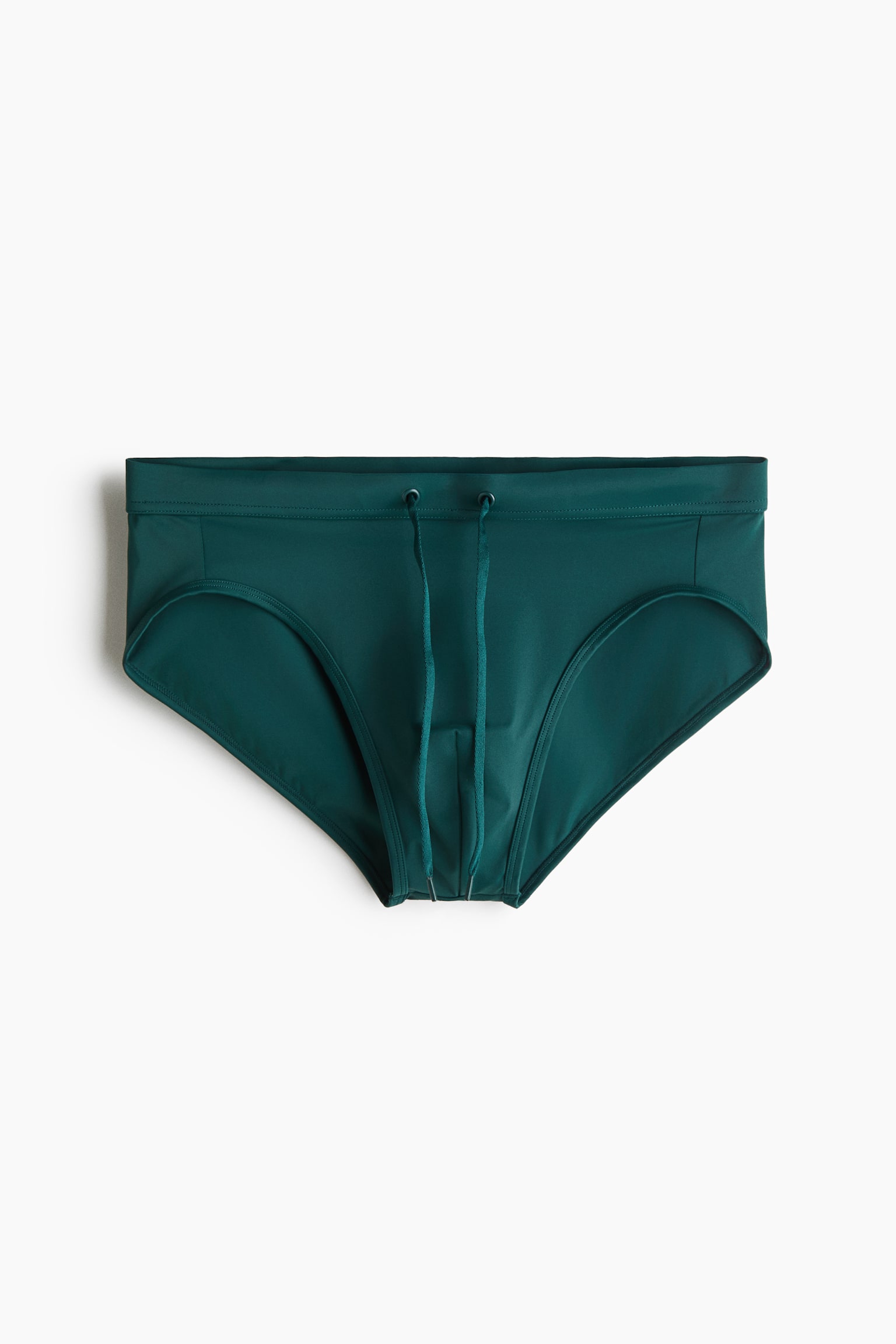 A pair of dark green swim briefs is shown from a front-facing angle, featuring an elastic waistband with two metal eyelets and a matching drawstring hanging down. The briefs are displaying a classic high-cut silhouette with tonal stitching.