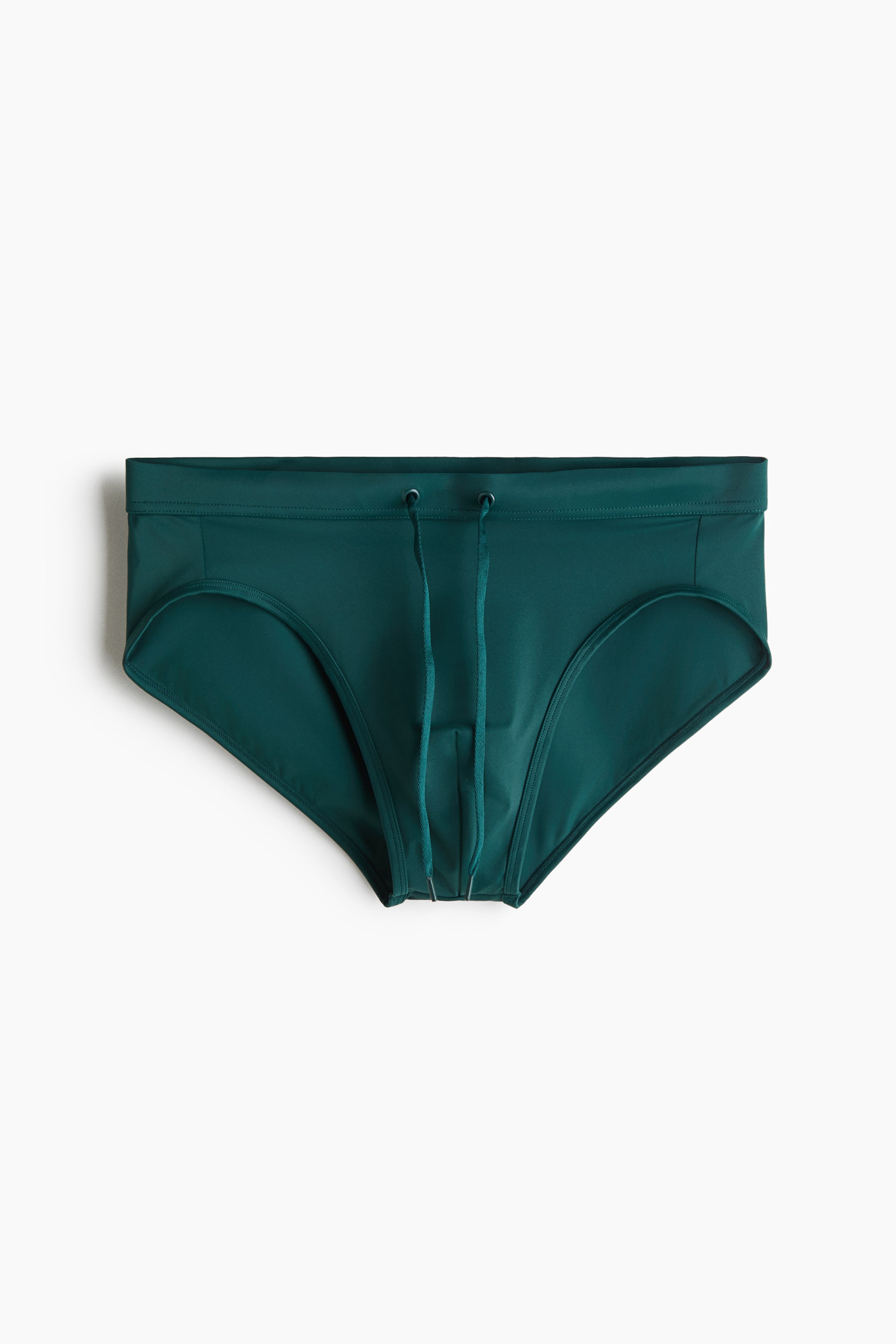 View larger image: A pair of dark green swim briefs is shown from a front-facing angle, featuring an elastic waistband with two metal eyelets and a matching drawstring hanging down. The briefs display a classic high-cut silhouette with tonal stitching.