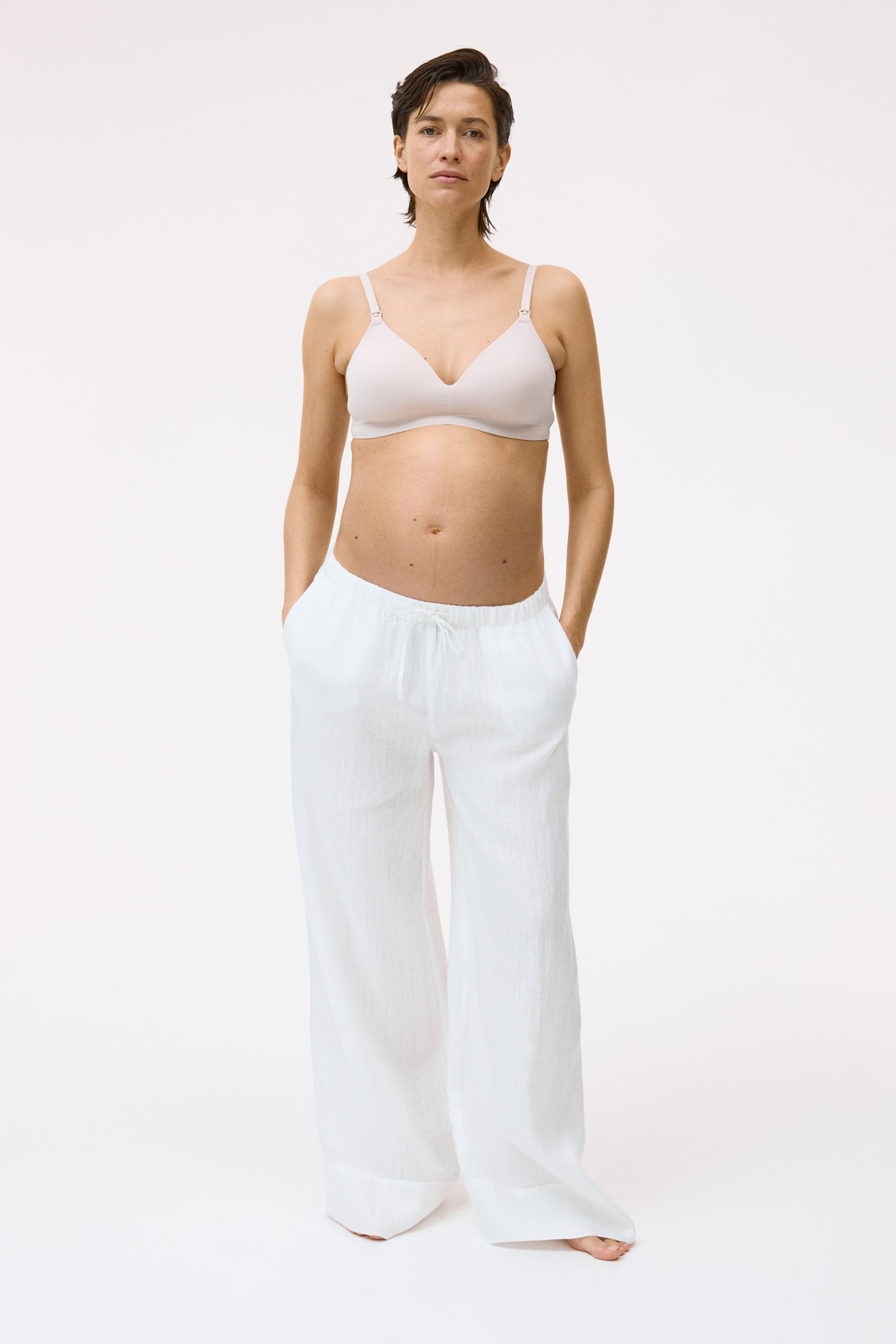 View larger image: The light pink bra features soft, unpadded, triangular cups and adjustable shoulder straps, with a small clip visible on each strap.
