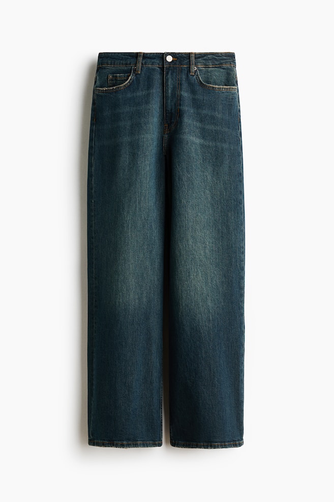 A pair of dark blue denim jeans is hanging vertically in a front view, showcasing a loose, straight-leg fit with a faded, worn-in wash along the thighs. The design features a regular waist with belt loops, a button fastening, and classic five-pocket styling with slightly distressed pocket edges. - 1
