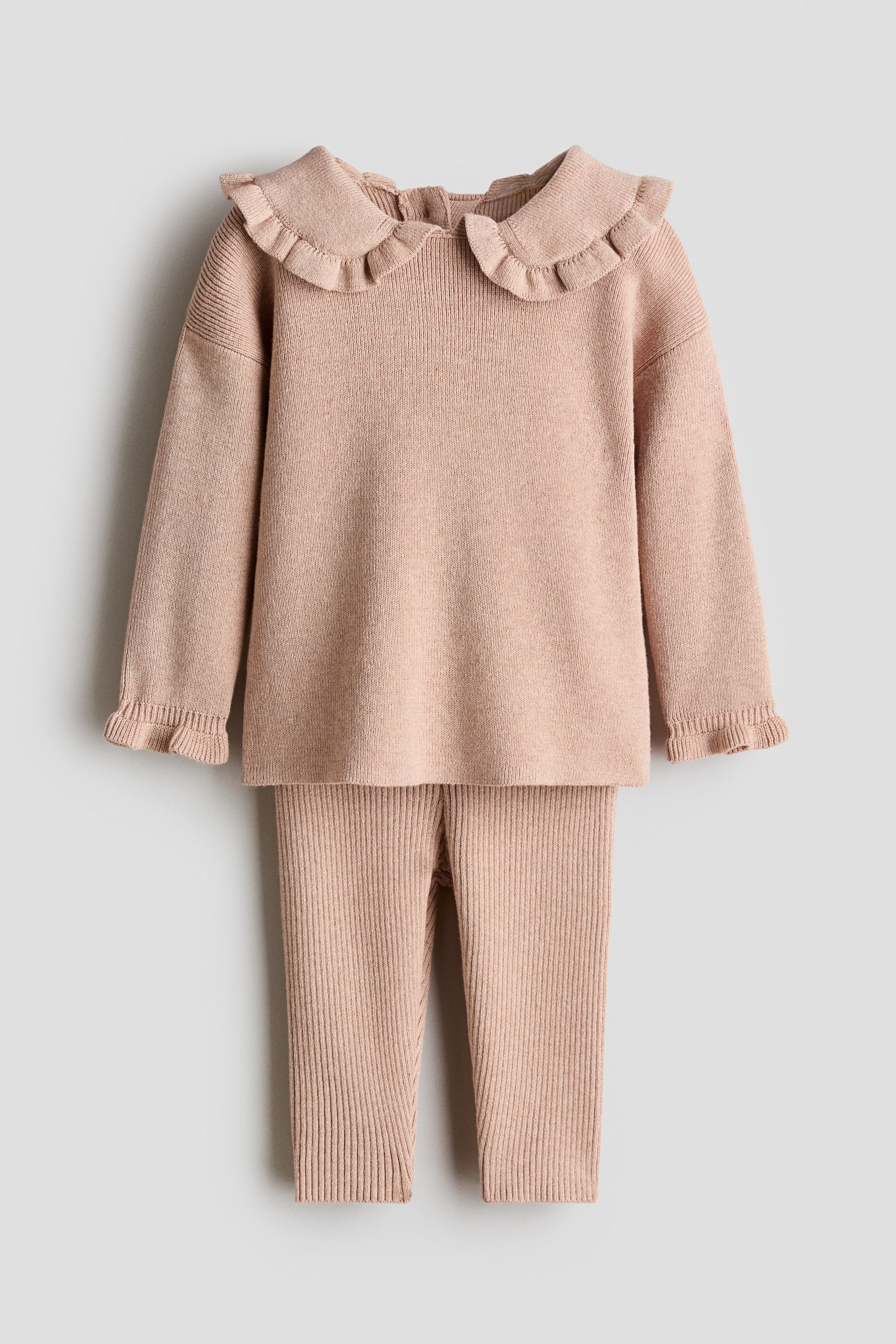 View larger image: An H&M Adorables two-piece set, in a pale pink soft rib-knit, is showcased laid flat, front-facing. The long-sleeved jumper features a round neckline with a frill-trimmed collar, dropped shoulders, and frilled cuffs, while matching ribbed leggings complete the set.