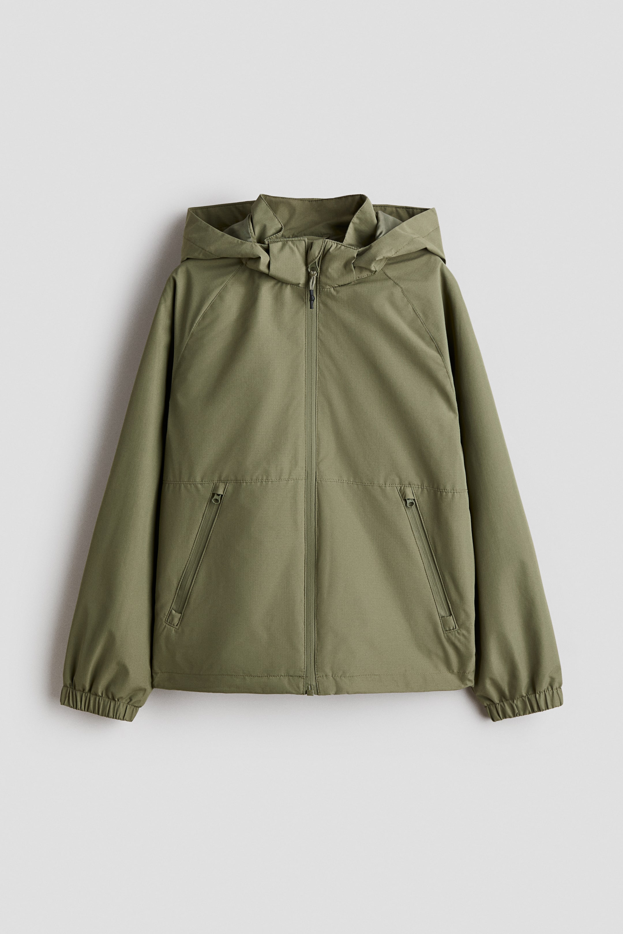 View larger image: A green shell jacket, facing front, features a hood, a stand-up collar, and a front zipper closure. Raglan sleeves, elasticized cuffs, two angled zippered side pockets, and an elasticized hem complete the design.