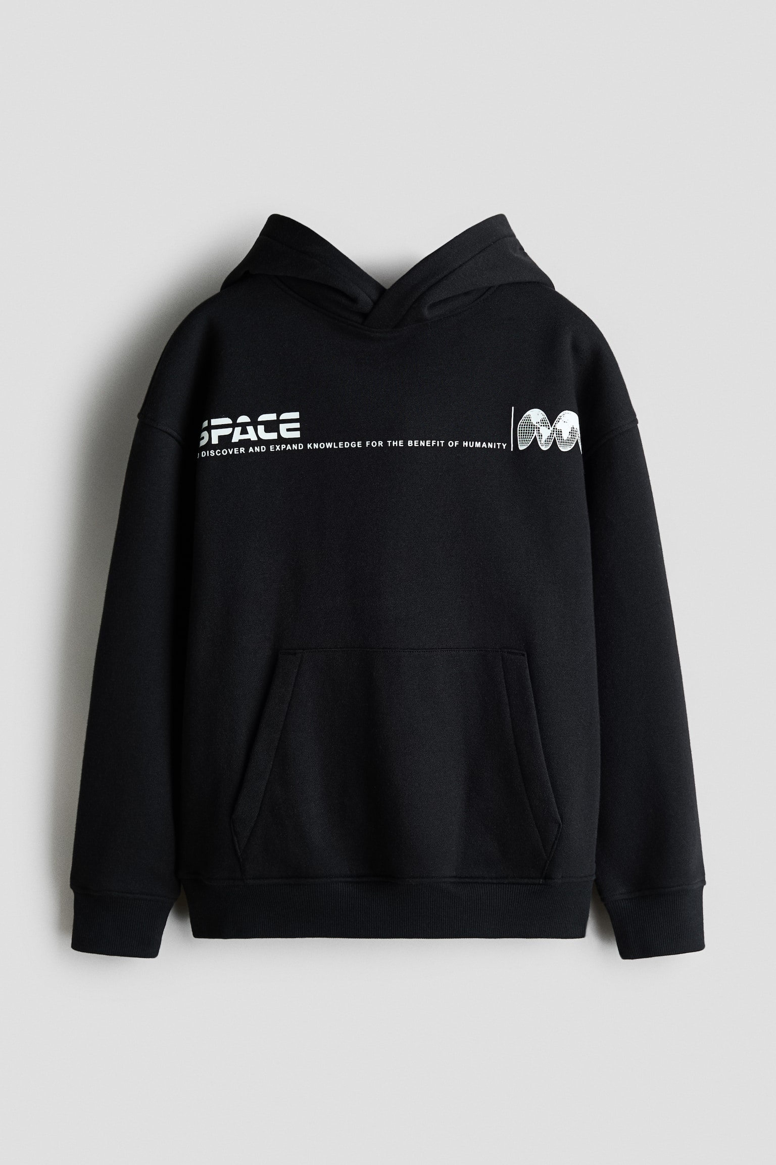 A black loose-fit hoodie is shown from the front, featuring a wrap-front hood, dropped shoulders, and a kangaroo pocket. It displays a white graphic print across the chest with the word "SPACE" alongside a line of text and a stylised globe design.