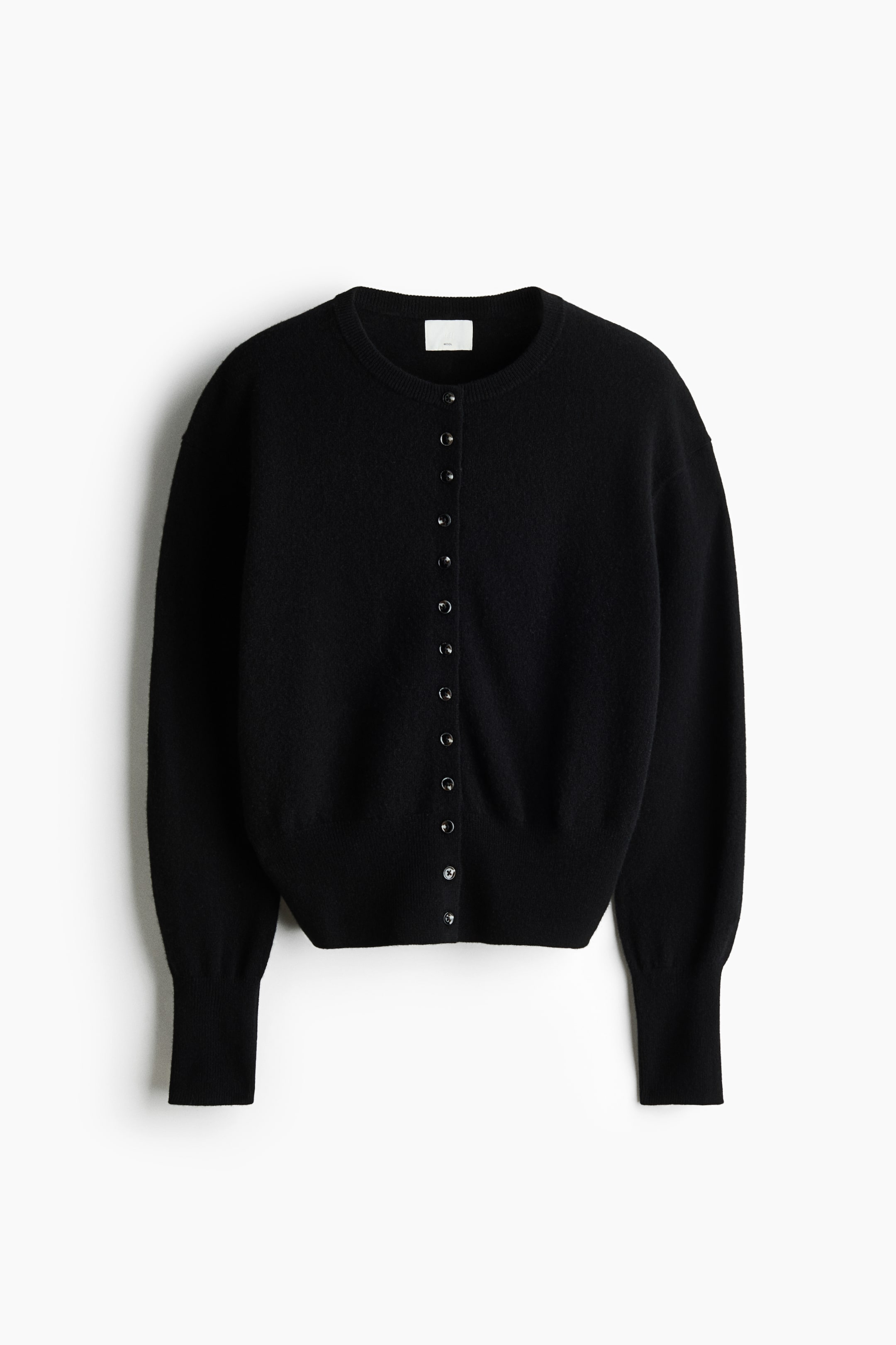 View larger image: A black knitted wool cardigan is shown from the front, featuring a round, rib-trimmed neckline and a row of small buttons running down the centre. It is displaying dropped shoulders, long sleeves with extended ribbed cuffs, and a ribbed hem.