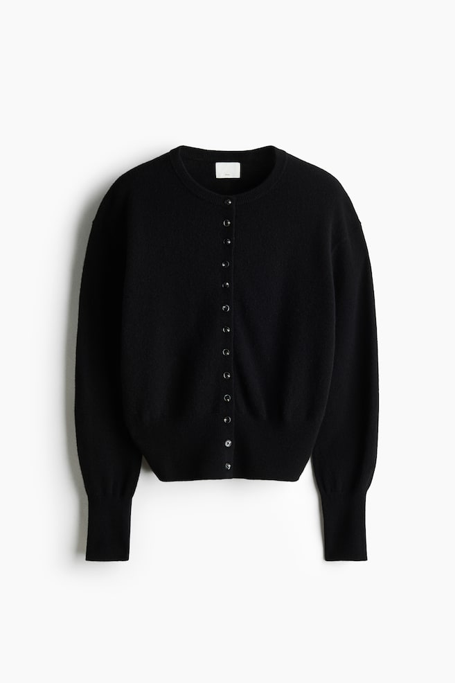 A black knitted wool cardigan is shown from the front, featuring a round, rib-trimmed neckline and a row of small buttons running down the center. It is displaying dropped shoulders, long sleeves with extended ribbed cuffs, and a ribbed hem. - 1