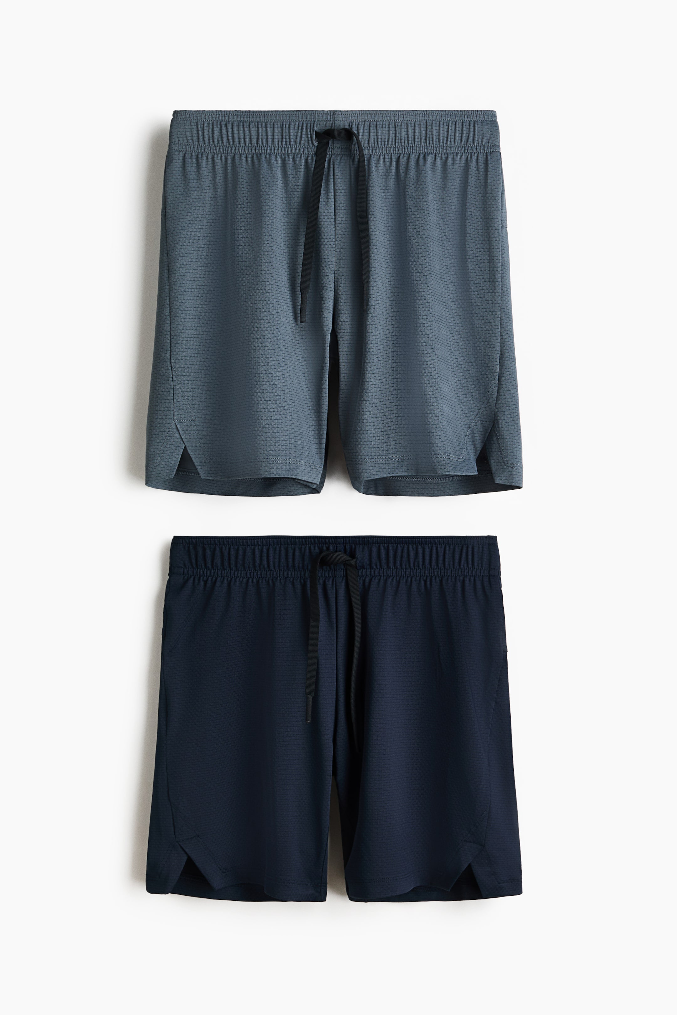 View larger image: A 2-pack of sports shorts is presented, with a grey-blue pair positioned above a dark blue pair. Both pairs feature a micro-perforated knit fabric, an elasticated waistband with a black drawstring at the front, and small side slits at the hem.