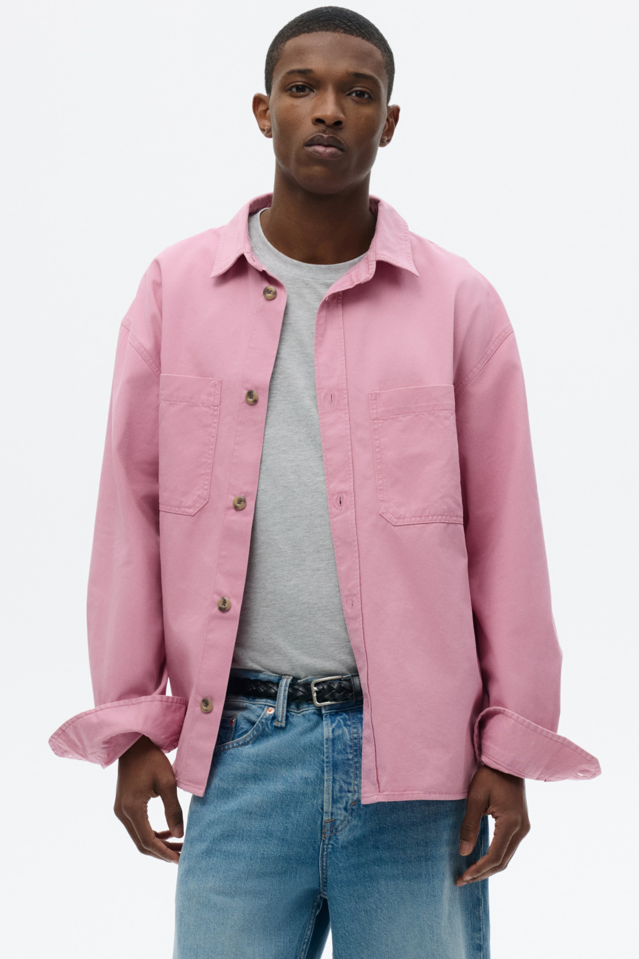 View larger image: A pink shirt jacket features a pointed collar and a button-up front with light-brown buttons, showcasing two chest patch pockets with flaps. Its long sleeves are rolled up at the cuffs, and it is worn open over a grey T-shirt, presenting a relaxed fit.