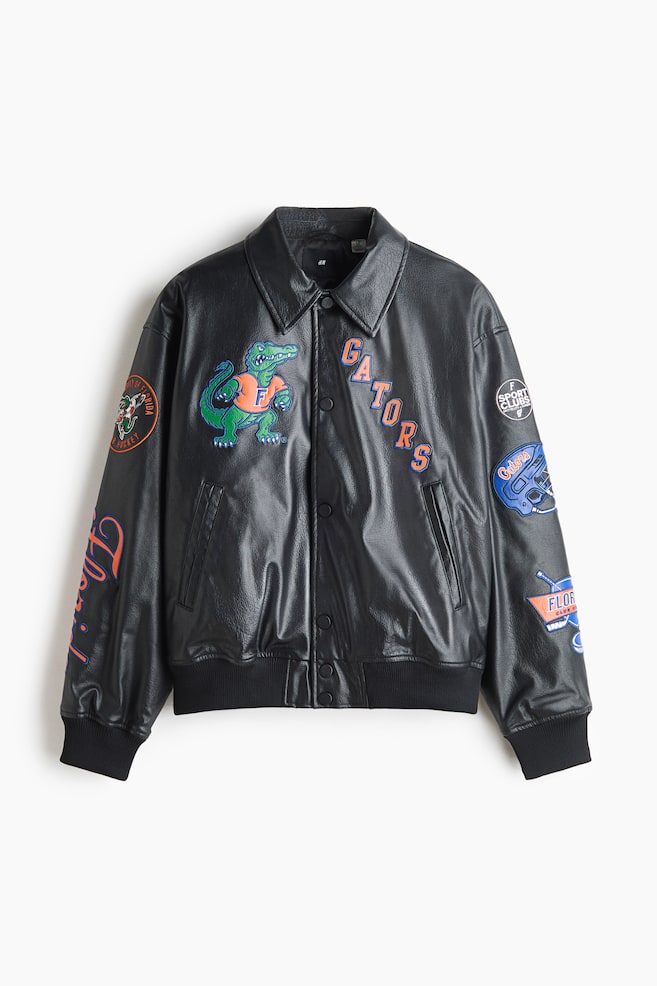 Eine schwarze Jacke aus Kunstleder ist von vorn zu sehen und verfÃ¼gt Ã¼ber einen spitzen Kragen, einen Druckknopfverschluss vorne, schrÃ¤ge Leistentaschen sowie RippbÃ¼ndchen an Ãrmeln und Saum. Die Jacke ist mit bunten Patches im Sport-Look verziert, darunter ein grÃ¼nes Alligator-Maskottchen auf der rechten Brust, das Wort âGATORSâ auf der linken Brust und verschiedene grafische Embleme entlang beider Ãrmel. - 1