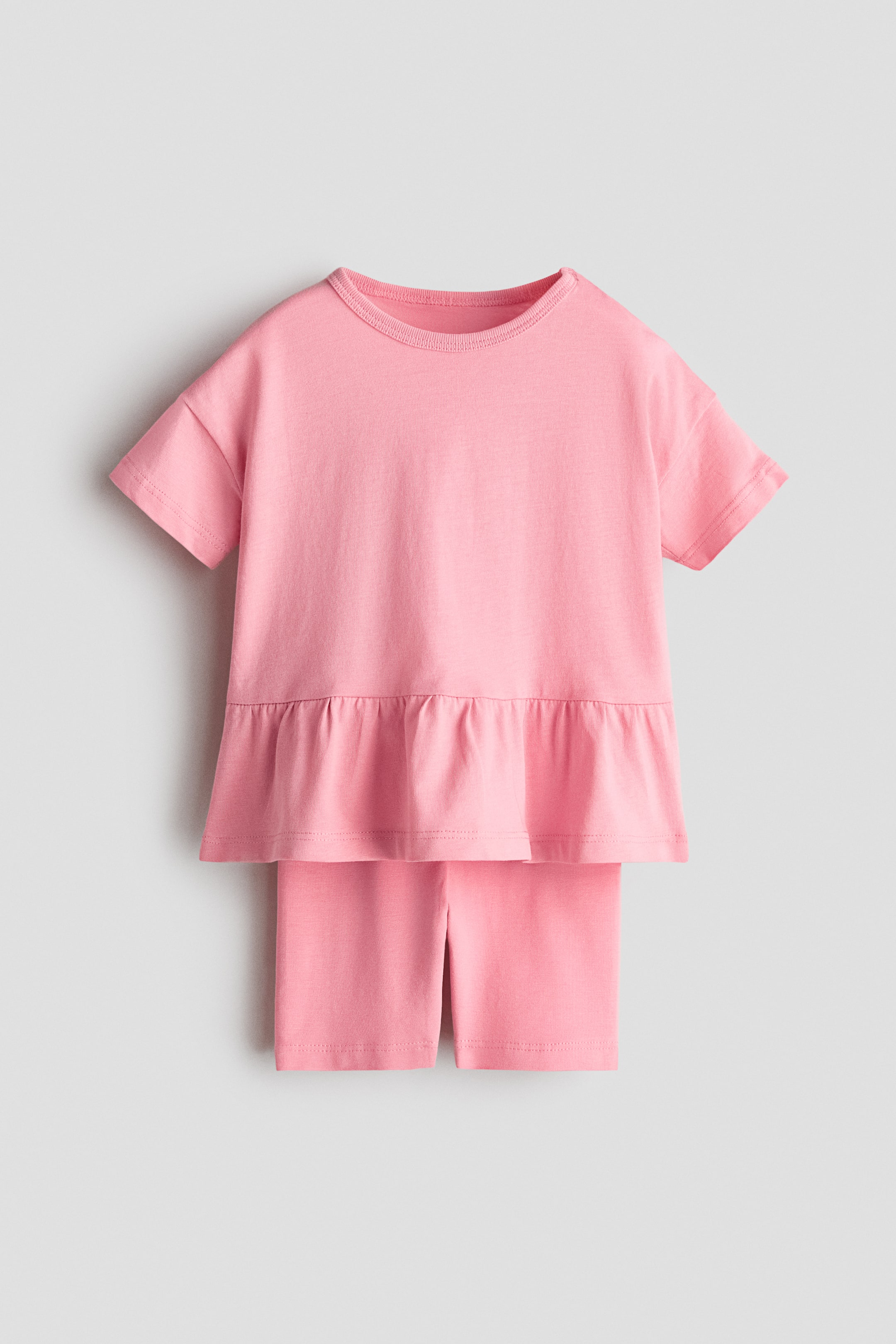 Grotere afbeelding bekijken: Een roze tweedelig setje wordt van voren gepresenteerd, met een top met korte mouwen, een geribbelde ronde hals en een geplooide peplumzoom, gecombineerd met bijpassende roze shorts.