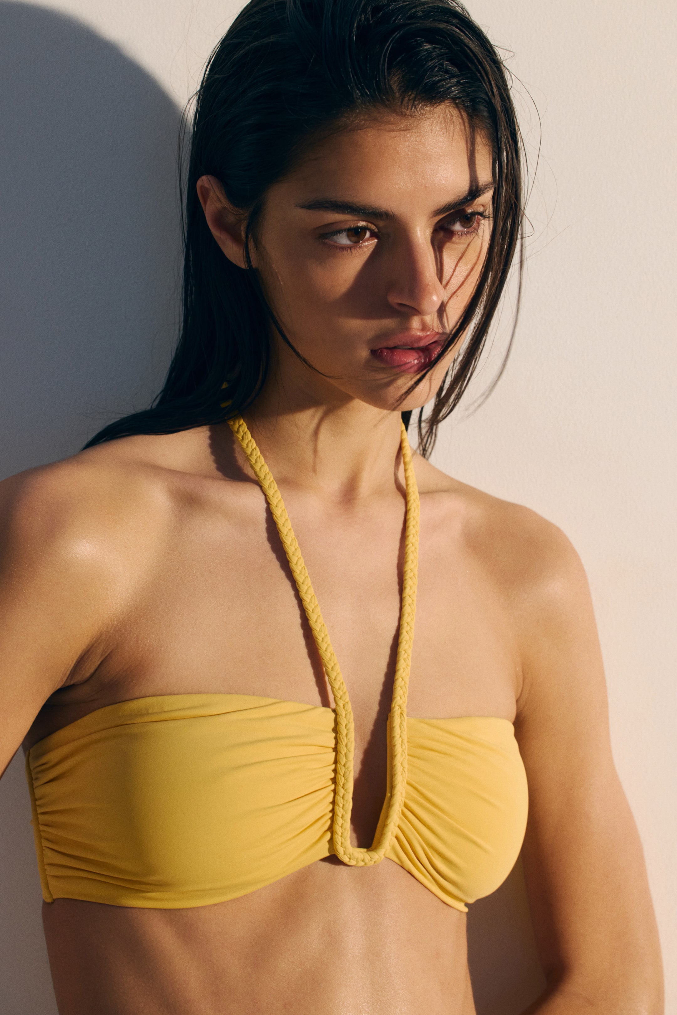 Ampliar la imagen: Top de bikini tipo bandeau amarillo con un frente fruncido y tirantes trenzados que forman una V en el centro. Se presenta desde el frente.