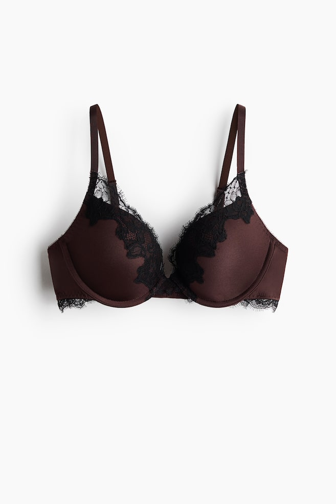 A dark brown bra showcasing smooth, padded cups and matching straps, adorned with black lace trimming along the top and bottom edges, creating an intricate overlay design on the upper cups. The bra is displayed from a front view. - 1