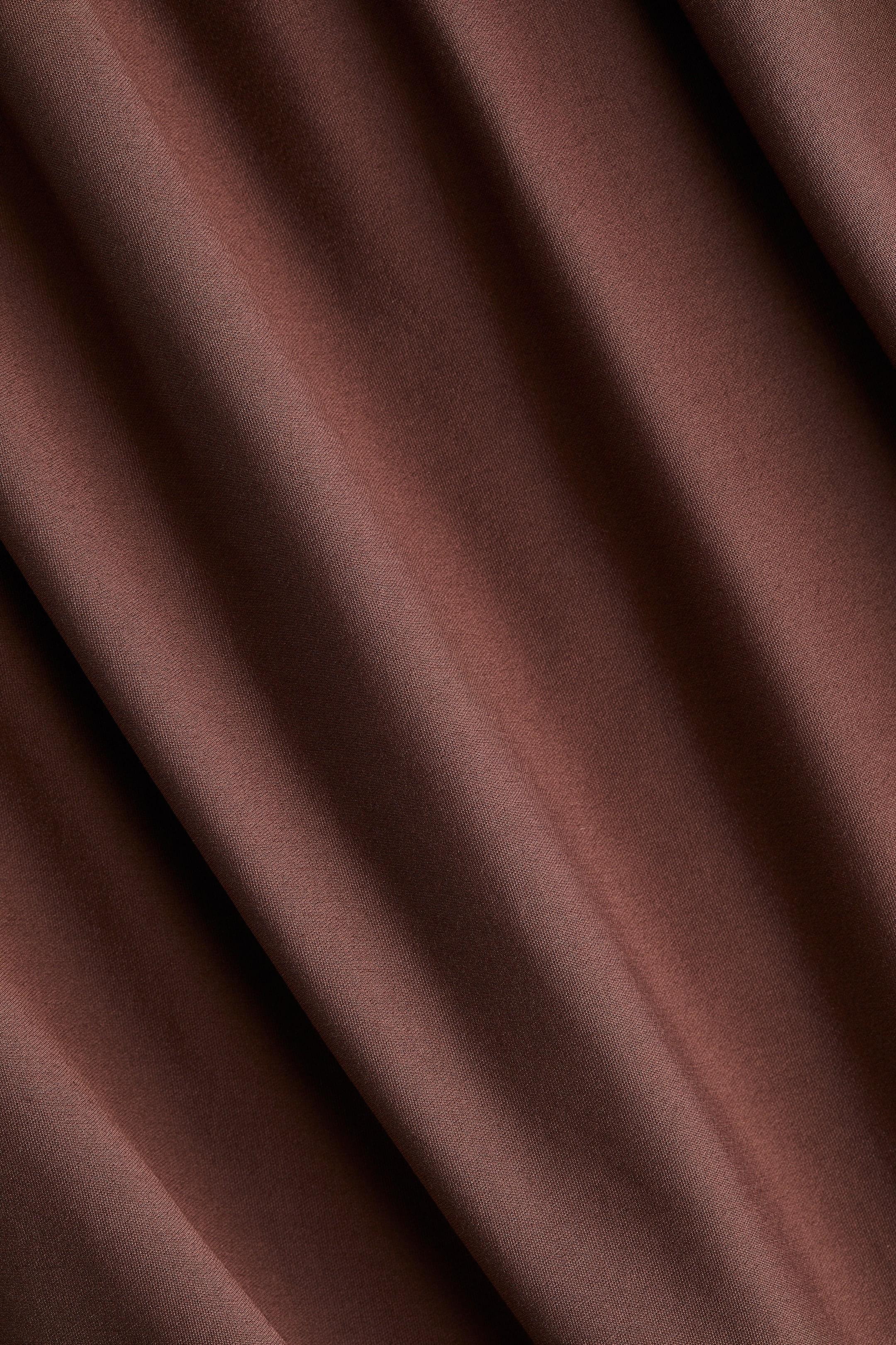 View larger image: A rich brown fabric is softly draped, revealing smooth folds and subtle textural variations as light plays across its surface.