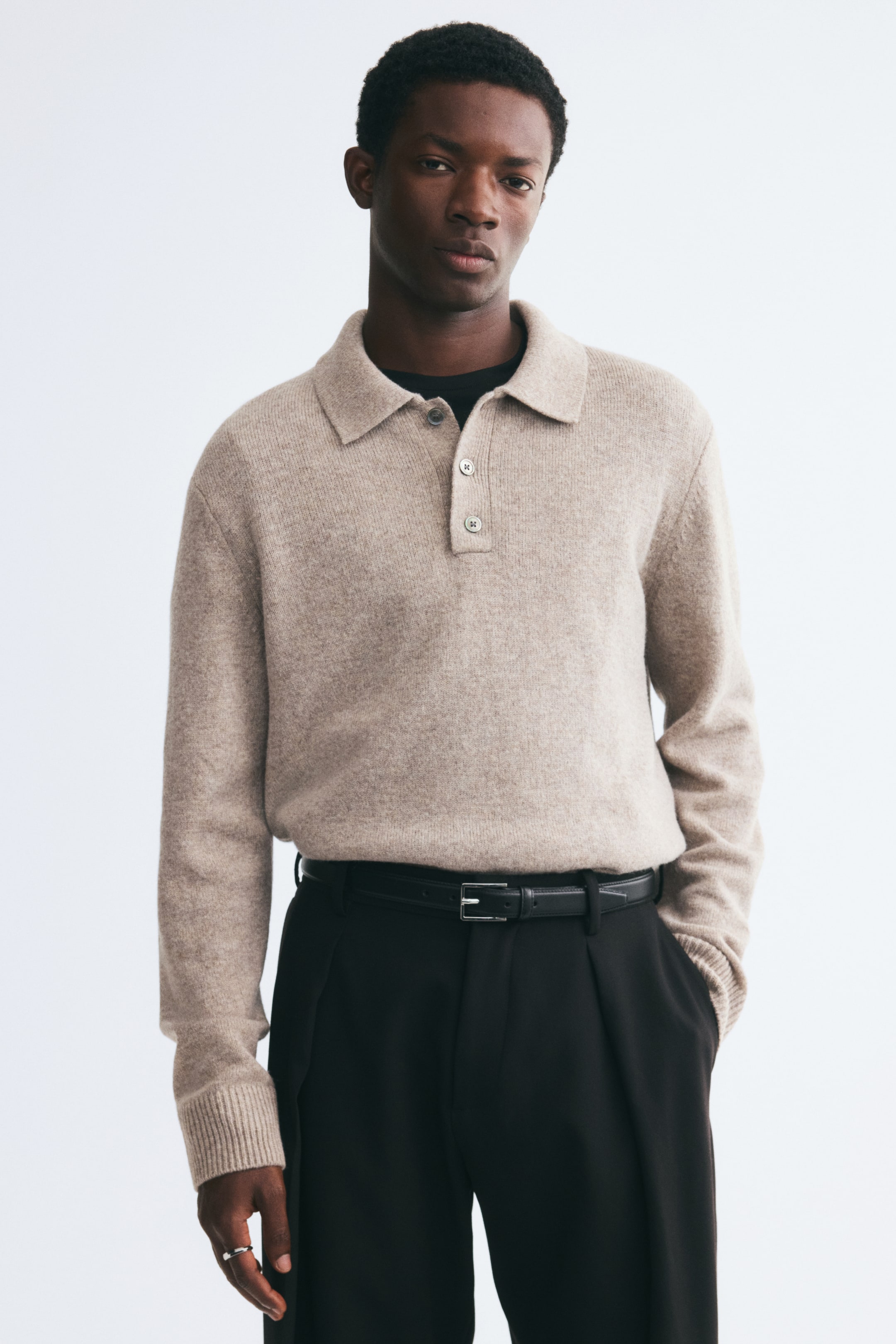 View larger image: A beige, fine-knit wool polo shirt is being worn by the model, tucked into black trousers secured with a black leather belt. The long-sleeve shirt features a classic collar, a partially open button placket, and ribbed cuffs, and is layered over a black crewneck T-shirt.