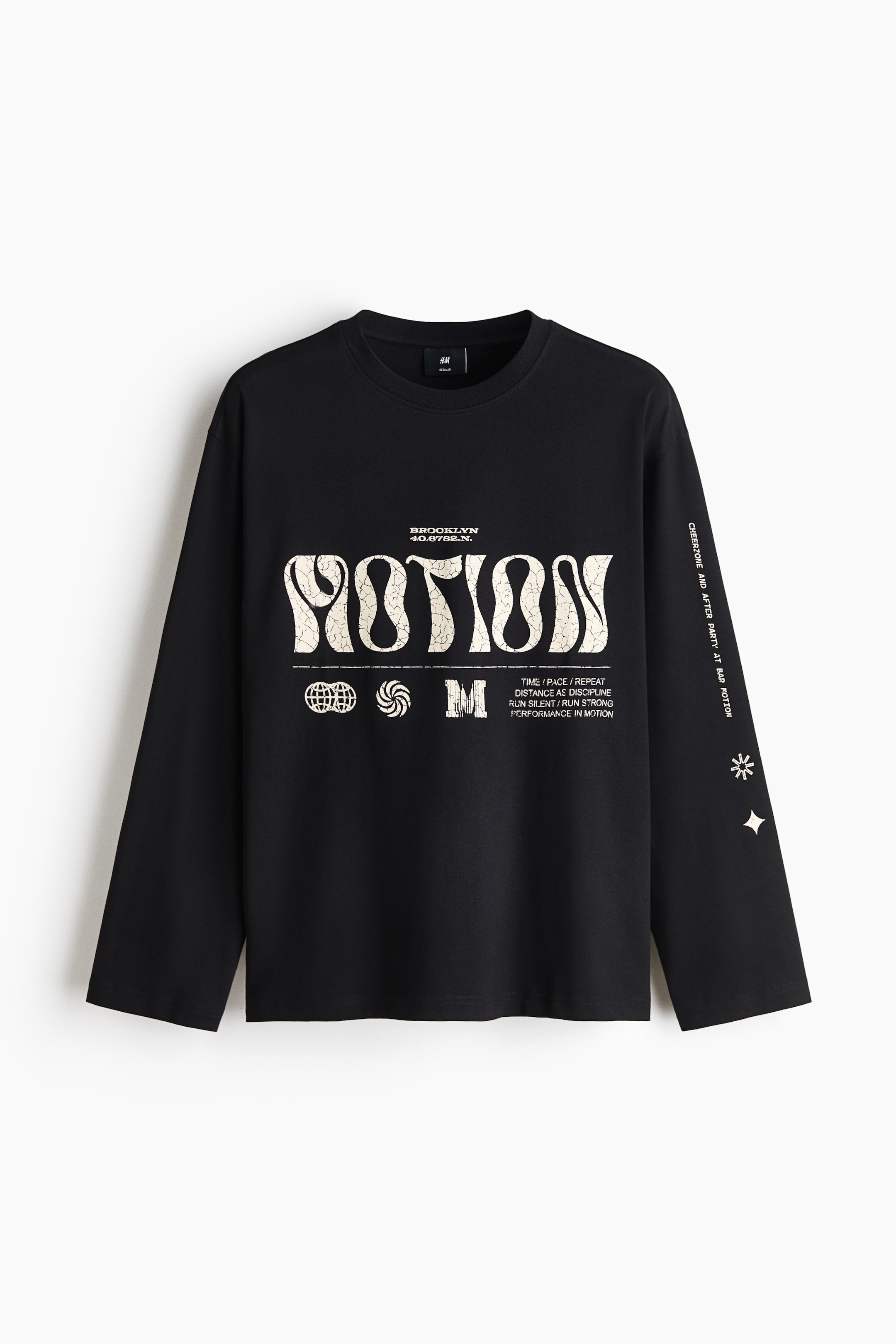 View larger image: A black long-sleeve crew neck T-shirt is laid flat, facing forward. It features a large distressed light beige 'MOTION' graphic on the chest, accompanied by smaller text and icons, including 'BROOKLYN' and 'PERFORMANCE IN MOTION'. The right sleeve also features vertical text and star graphics.