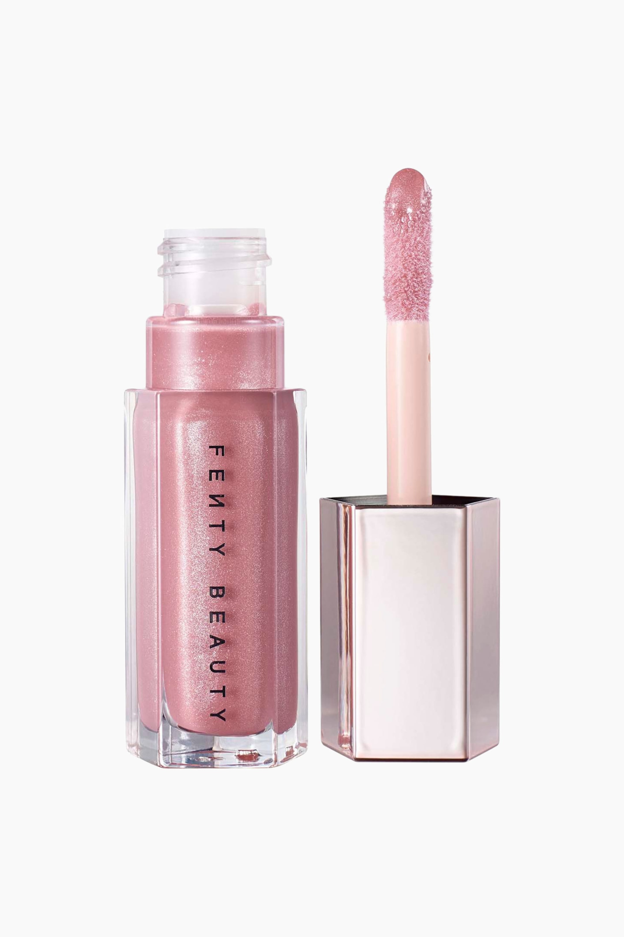 Visa större bild: En öppnad flaska med Fenty Beauty läppglans i en skimrande rosapink nyans står upprätt bredvid sitt avskruvade lock. Den sexkantiga, genomskinliga behållaren visar vertikal svart varumärkestext, medan det metalliskt roséguldfärgade locket håller applikatorpinnen uppåt för att visa den glansbelagda doe-foot-spetsen.