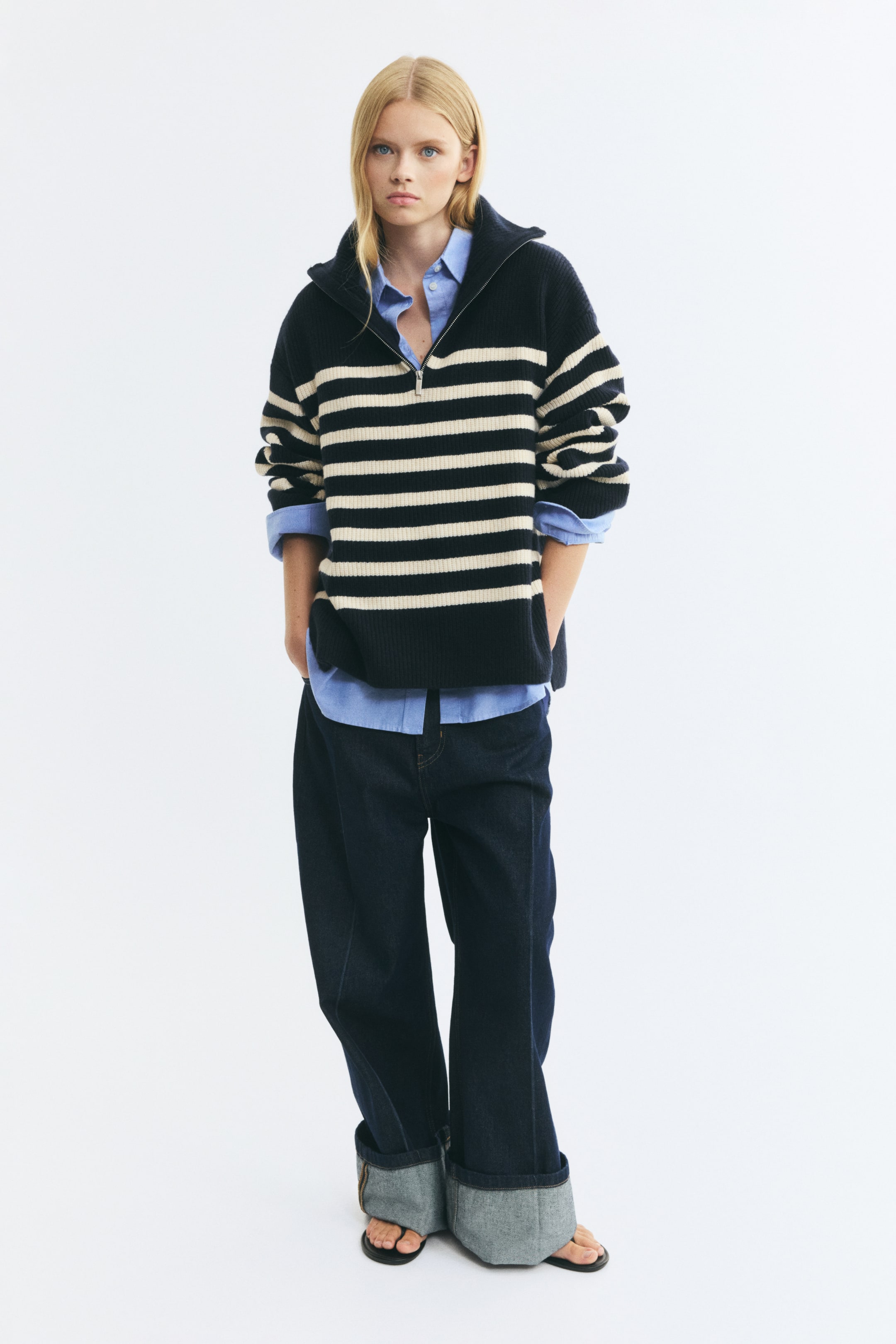Größeres Bild anzeigen: Das Modell trägt einen gestreiften Half-Zip-Pullover aus englischem Rippenstrick in Dunkelmarine und Creme. Der Pullover verfügt über einen offenen Stehkragen, überschnittene Schultern und weite Ärmel und ist über einem hellblauen Hemd mit Kragen und dunklen Wide-Leg-Jeans getragen.