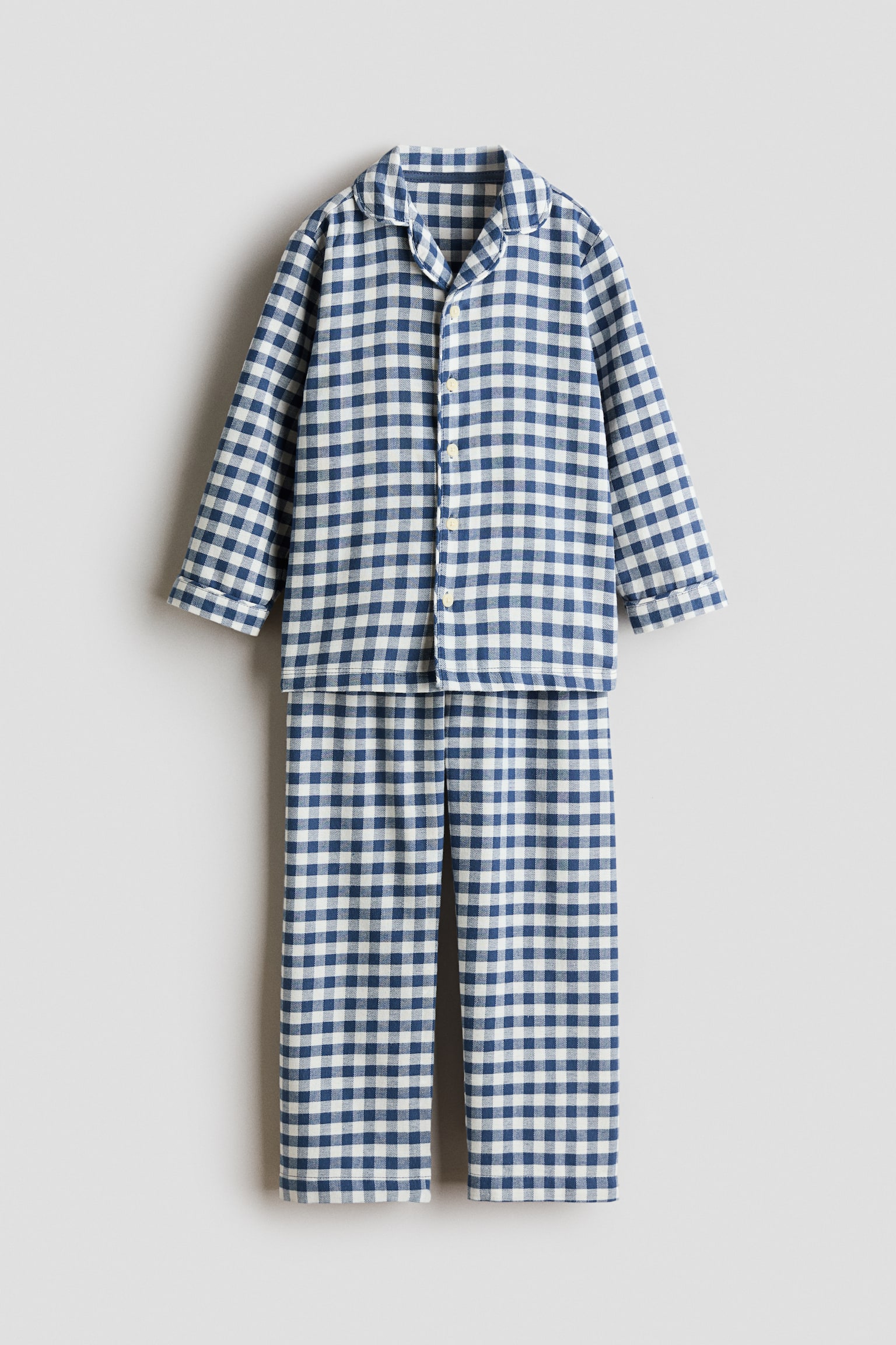 Et blÃ¥t og hvidt pyjamassÃ¦t i gingham hÃ¦nger set forfra og bestÃ¥r af en langÃ¦rmet skjorte med knapper og reverskrave samt matchende bukser med lige ben. - 1