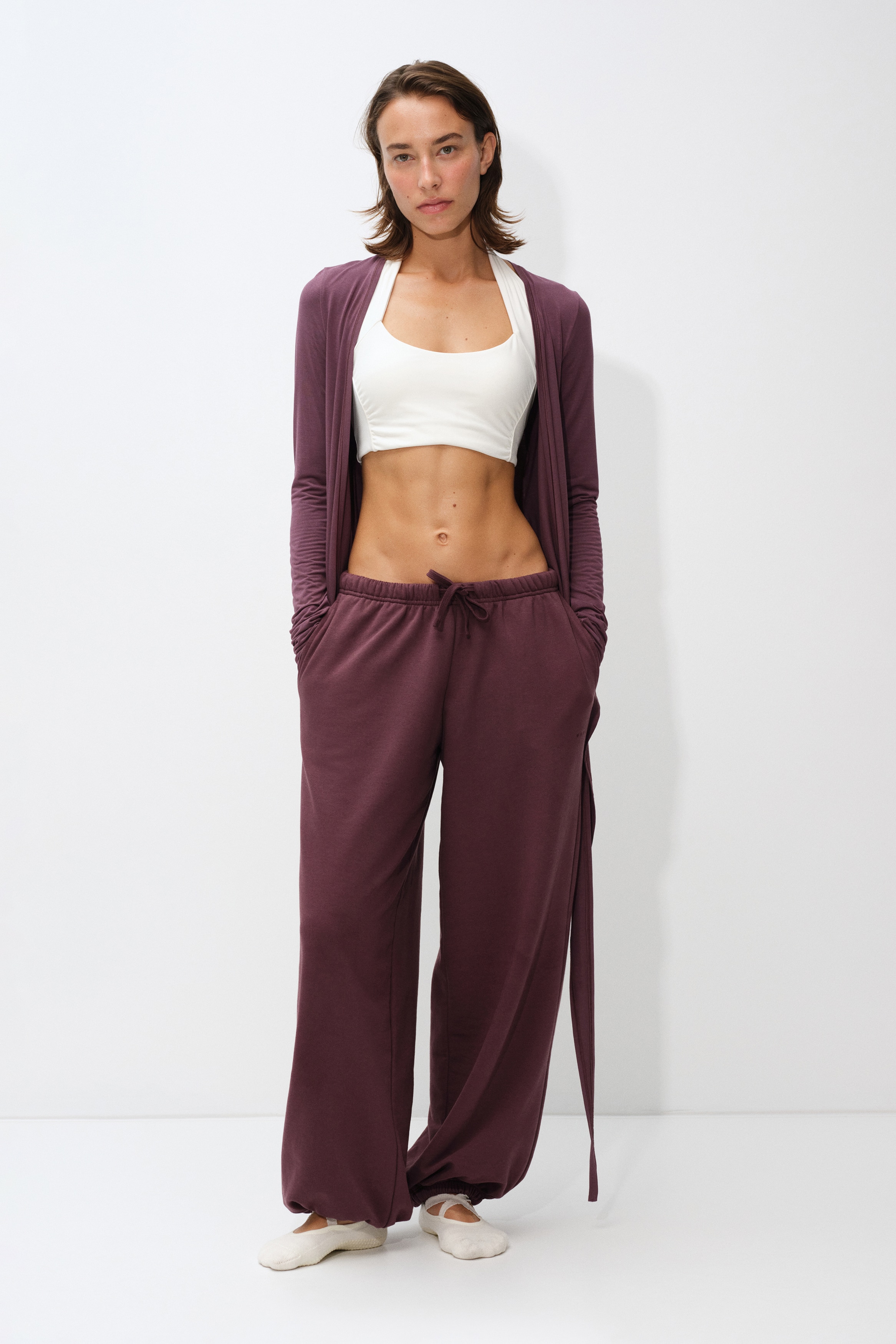 A pair of burgundy joggers is hanging front-facing, showcasing an elasticated waistband with a matching drawstring and relaxed-fit legs that finish in gathered elastic cuffs.