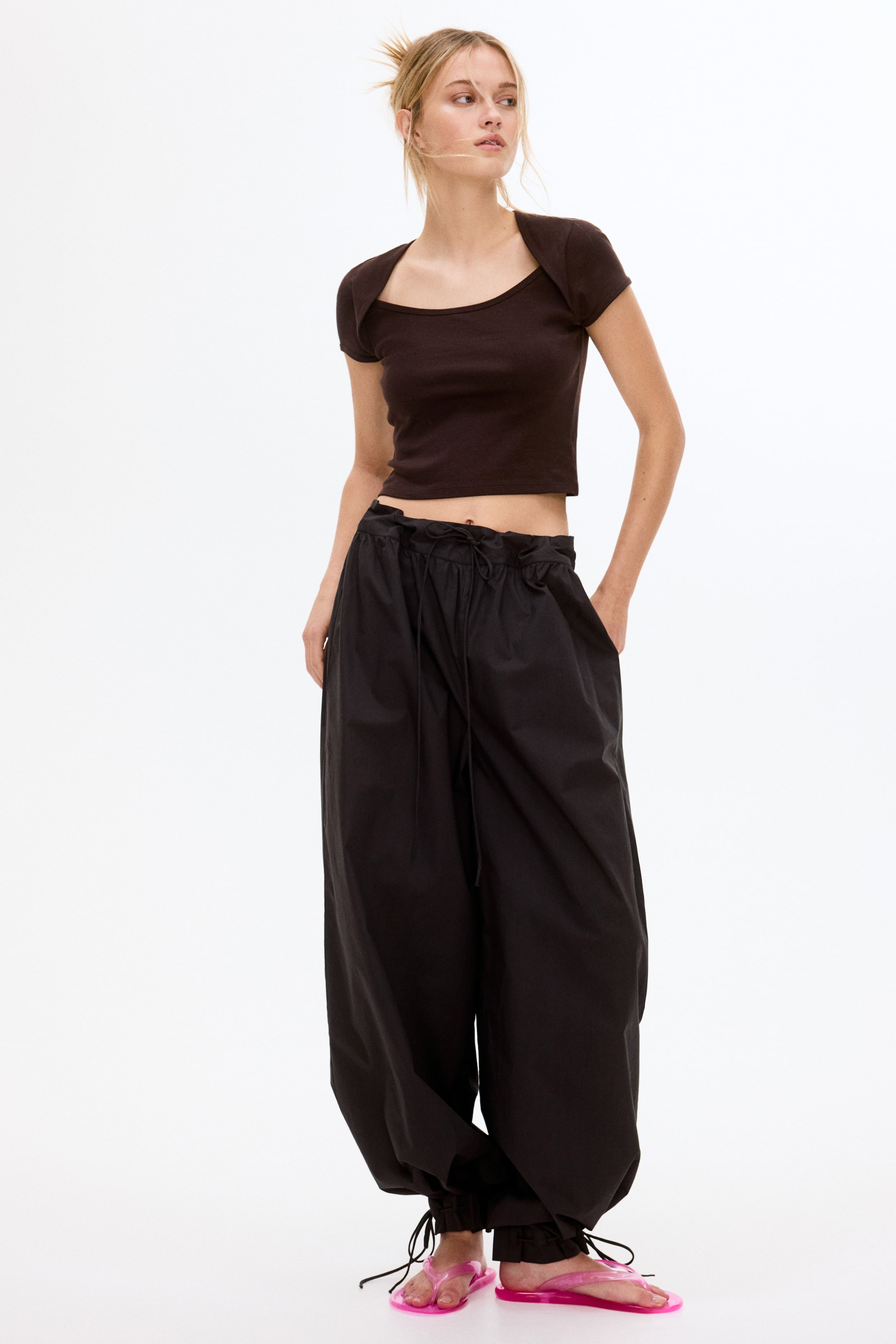 View larger image: A dark brown cropped top features a scoop neckline with wide shoulder straps and short sleeves, fitting snugly. Black baggy pants showcase an elasticated drawstring waist, voluminous legs, and cinched ankles with ties, presented from a slight front-left angle.