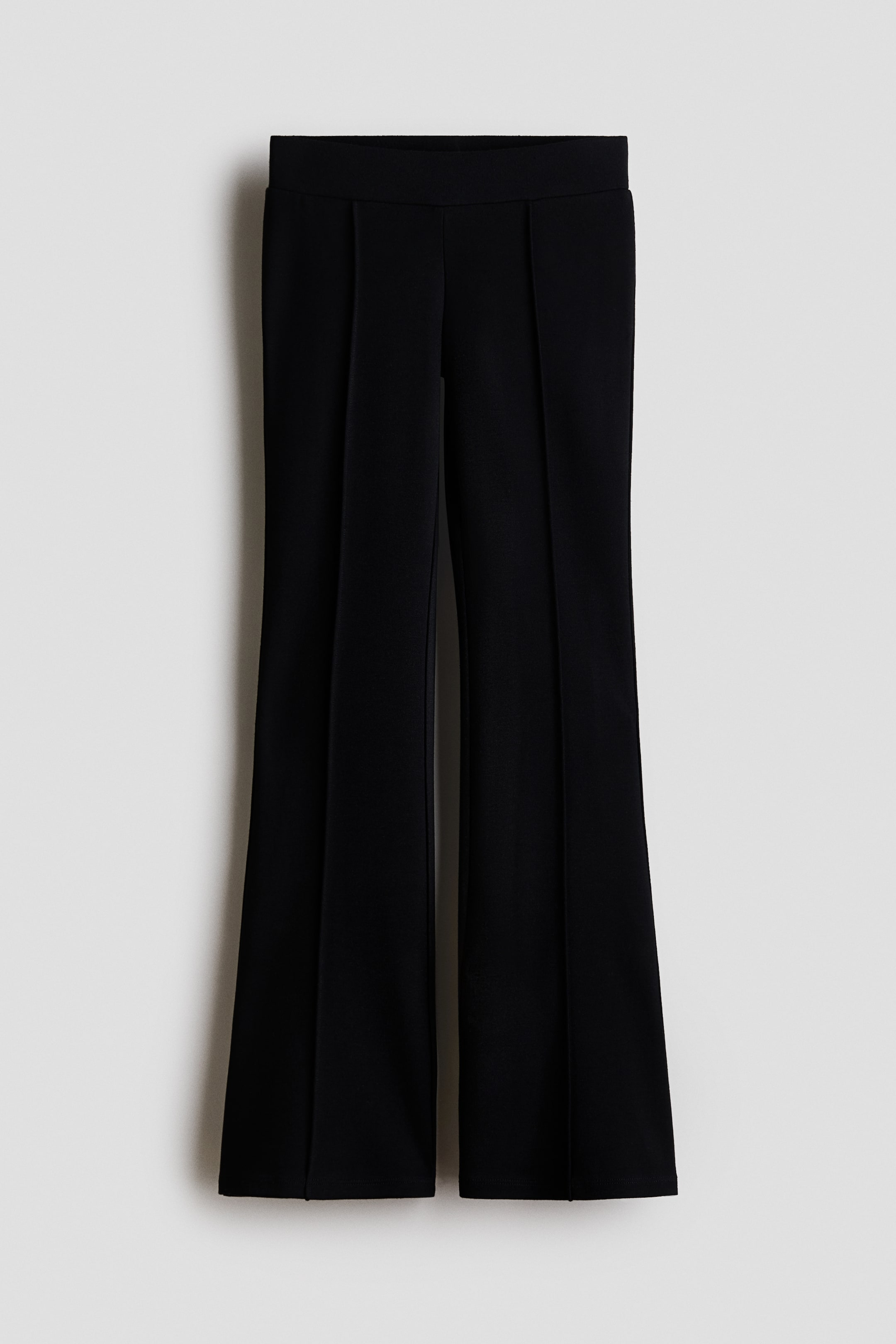 View larger image: Black trousers are featuring a flat waistband and vertical stitched creases running down the front of each leg, flaring subtly from the knee to the hem.