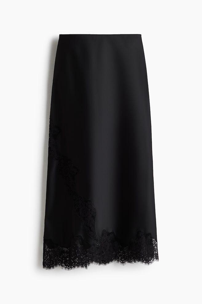 A black satin midi skirt is hanging front-facing, showcasing a smooth, lustrous drape. It features a diagonal insert of black floral lace on the lower left side, which connects to a scalloped eyelash lace hem. - 1