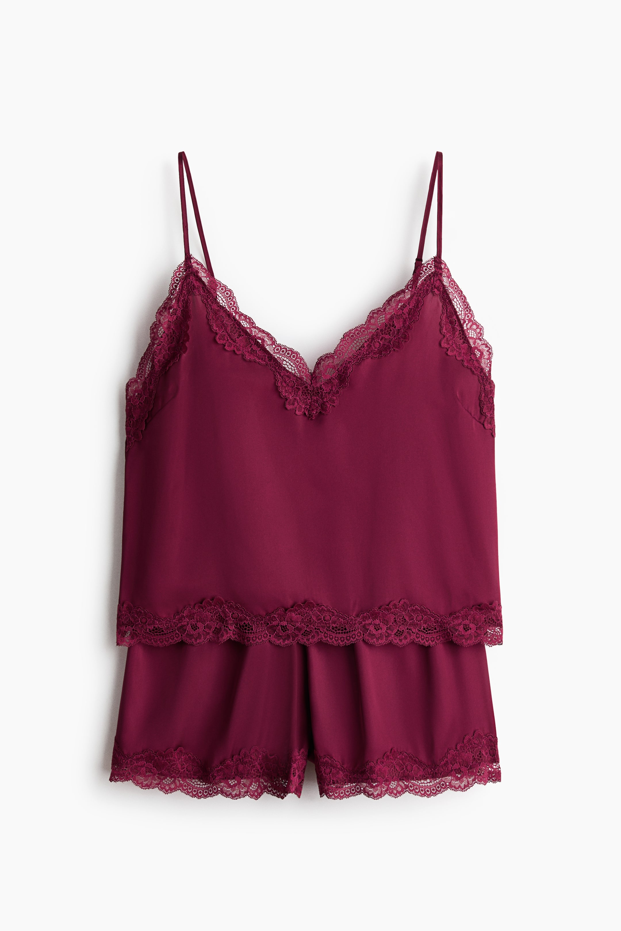 View larger image: A deep red, softly draping satin pyjama set is showcased at the front, featuring a strappy top with spaghetti shoulder straps and a V-shaped neckline, both adorned with lace trimming. The matching shorts come with an elasticated waist and lace trims along the hem.