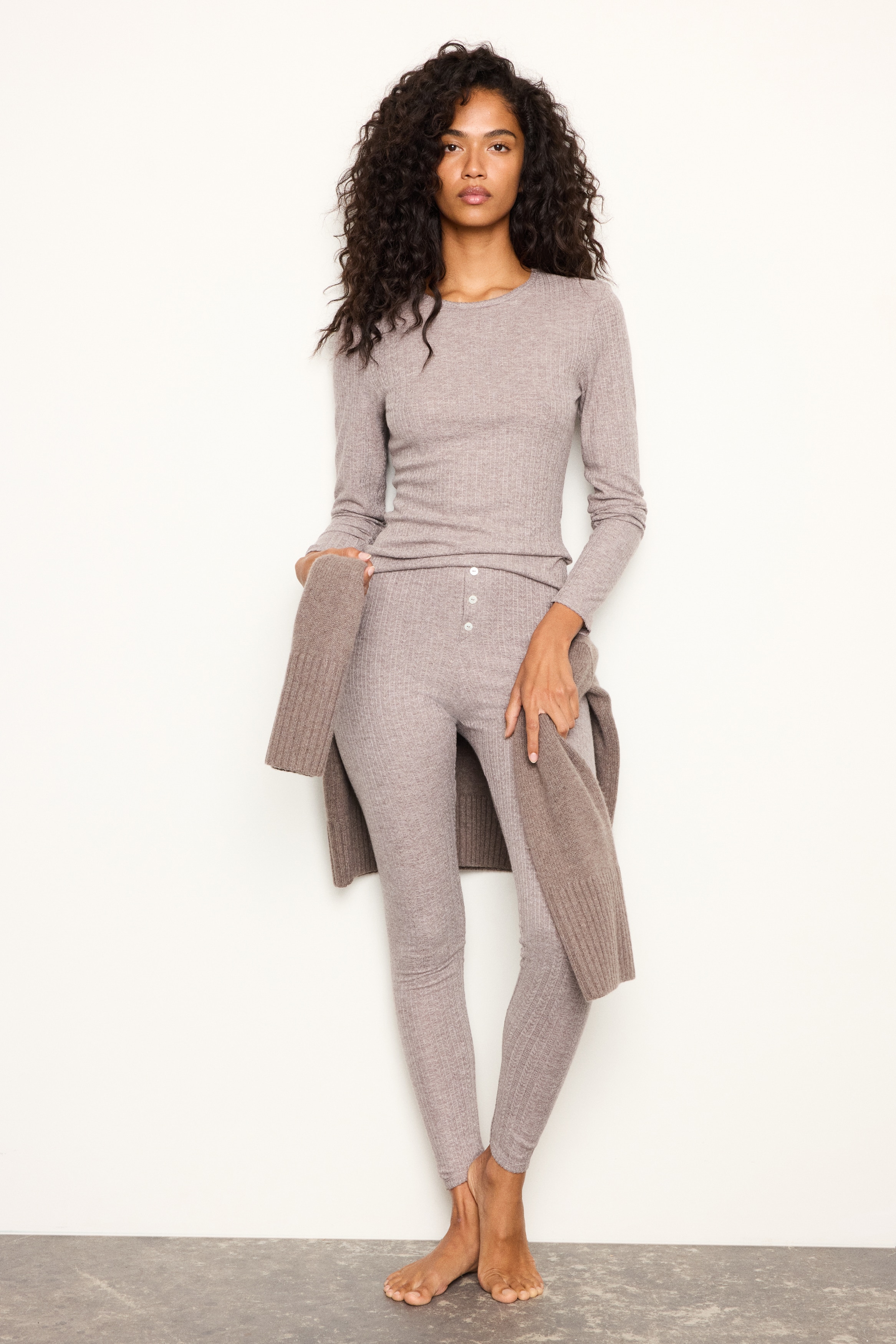 Un pigiama due pezzi in jersey pointelle testurizzato color tortora Ã¨ mostrato frontalmente, composto da un top a maniche lunghe e da leggings slim fit coordinati. Il top presenta uno scollo rotondo e entrambi i capi mostrano delicati dettagli di finitura picot sullo scollo, sui polsini e sugli orli.