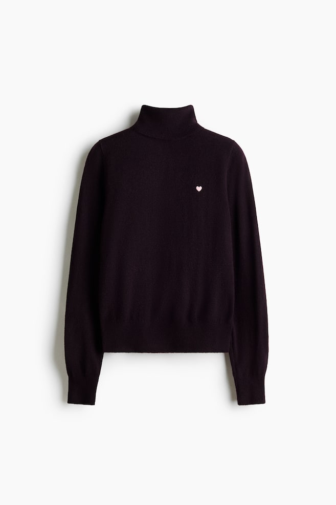 Un pull Ã  col roulÃ© violet foncÃ©, vu de face, avec un petit cÅur rose brodÃ© sur la poitrine gauche. Il prÃ©sente des manches longues avec des poignets cÃ´telÃ©s et un ourlet cÃ´telÃ©. - 1