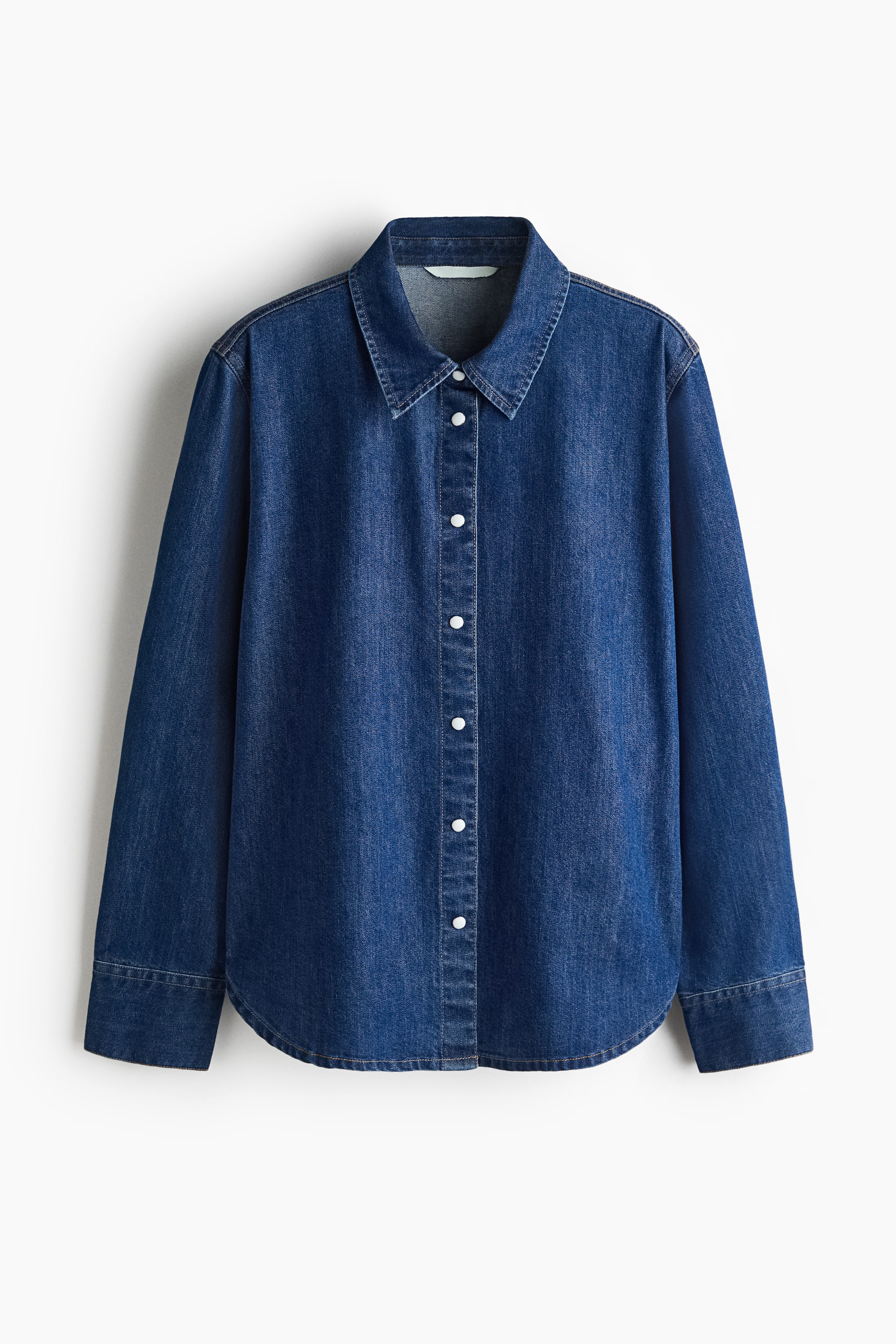 View larger image: A blue denim shirt is shown front-facing, featuring a pointed collar, a full button-front closure with white buttons, long sleeves with single buttoned cuffs, and a rounded hem.