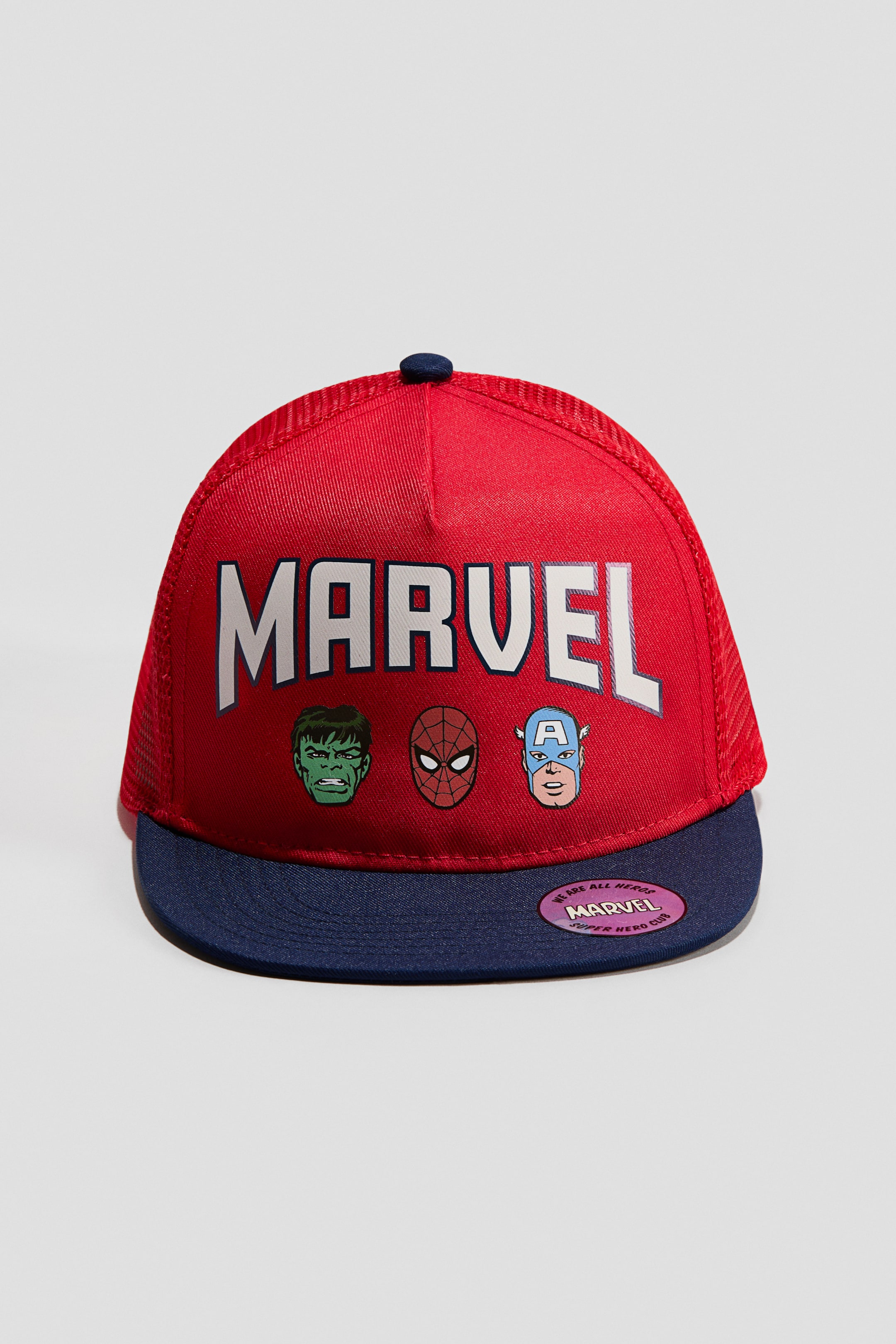 View larger image: A red and blue trucker cap is facing FRONT, featuring "MARVEL" text in white across the solid red front panel. Images of Hulk, Spider-Man, and Captain America are appearing below the text, while a pink circular sticker with "MARVEL" branding is adhering to the blue brim.