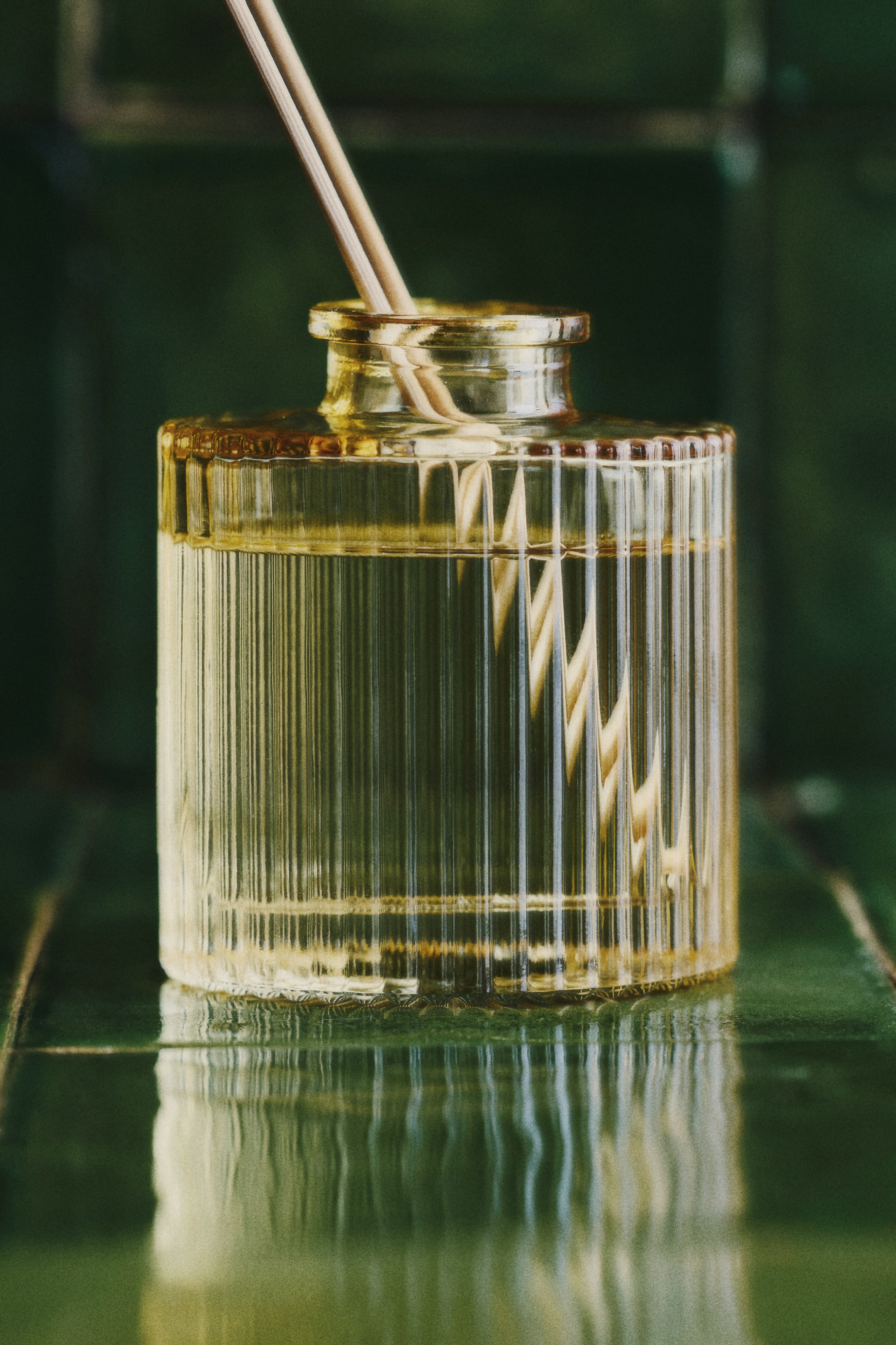 View larger image: A front-facing diffuser bottle, crafted from fluted, amber-tinted glass, contains a clear oil. Several light-colored wooden reeds stand in the oil, extending from the bottle's neck.