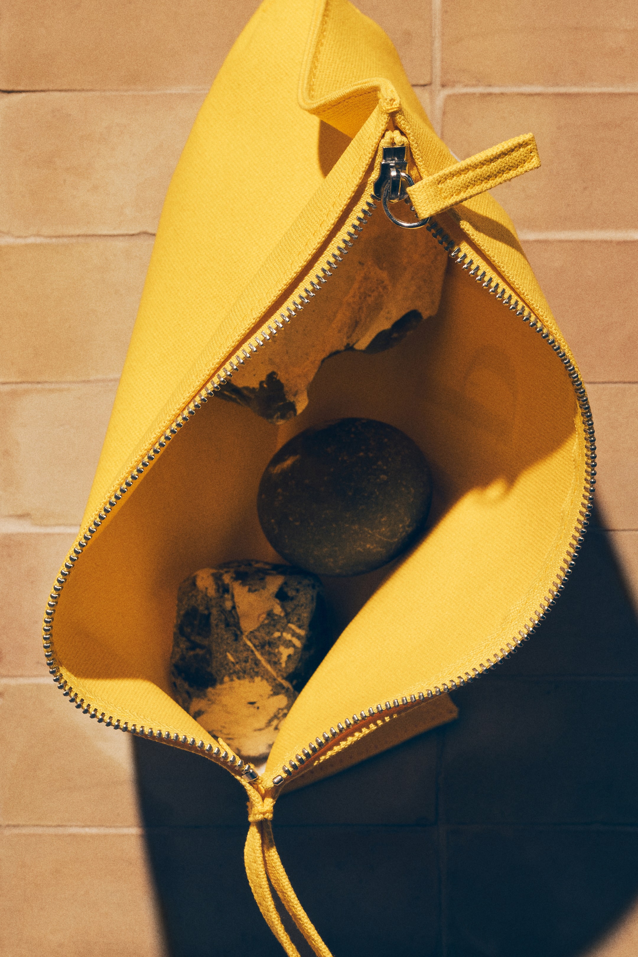 View larger image: A yellow fabric pouch is angled downwards, its top opening widely and featuring a silver-toned zipper with a fabric pull tab and a yellow cord tied at the bottom of the zipper track. The pouch's interior is holding three natural stones, showcasing its capacity.