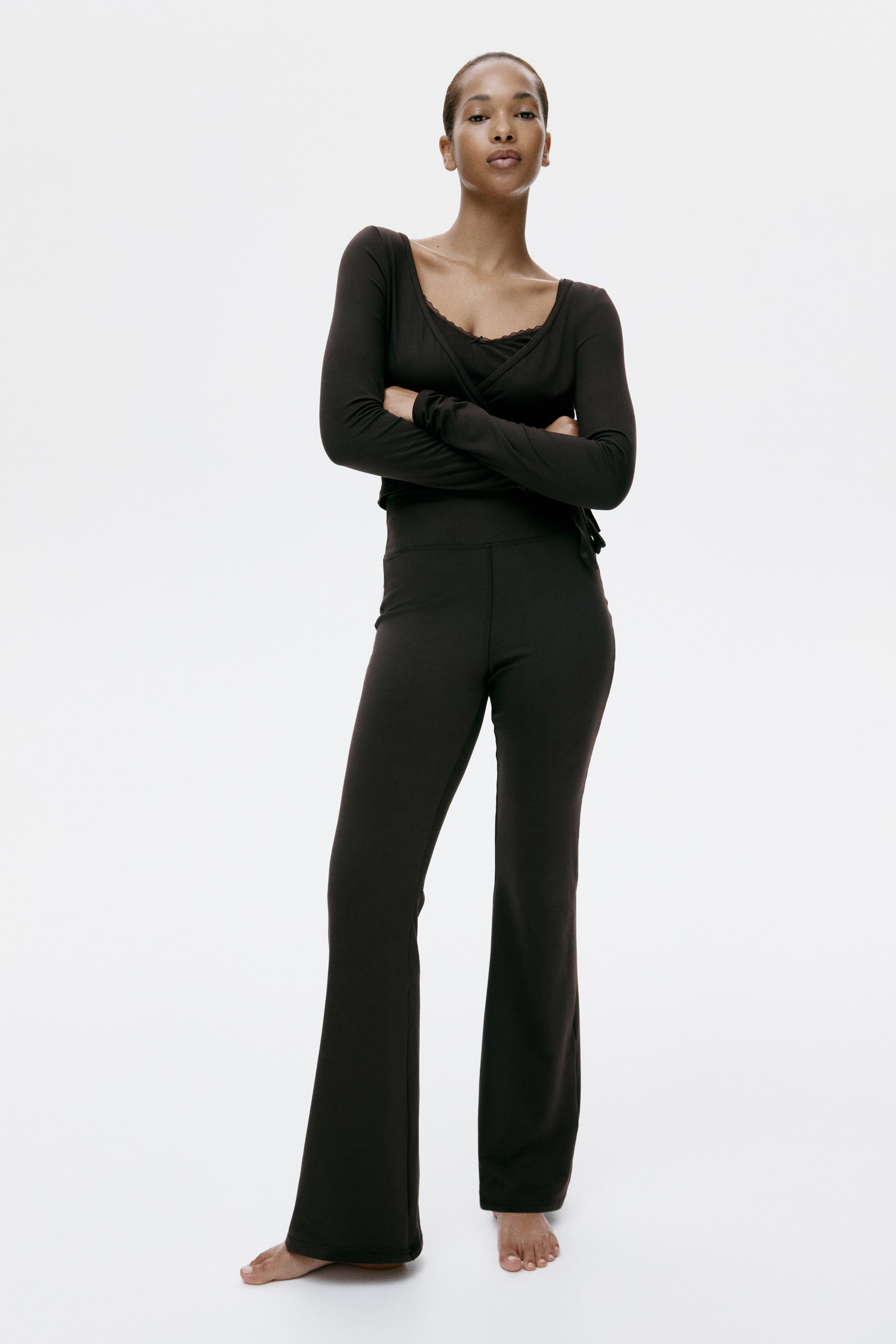 View larger image: Fitted trousers in brushed stretch-jersey, featuring a wide waistband and flared legs, are shown on the model. These trousers fit closely through the hips and thighs before flaring out from the knees.