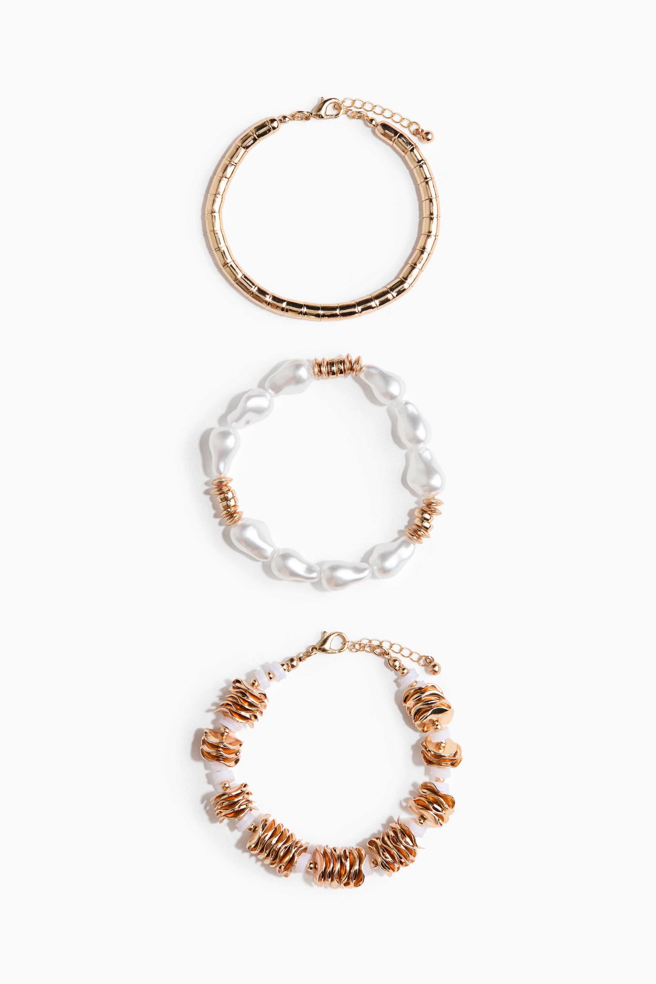 Visa större bild: Tre armband ligger platt, framåtvända. Det översta armbandet presenterar en guldfärgad, segmenterad ormkedjedesign med en hummerlås. Det mellersta armbandet har oregelbundna vita barockpärlor som alternerar med små guldfärgade räfflade tunnpärlor. Det nedersta armbandet visar ljusrosa sfäriska pärlor som är utspridda med större vågiga guldfärgade tunnpärlor, säkrade med en hummerlås.