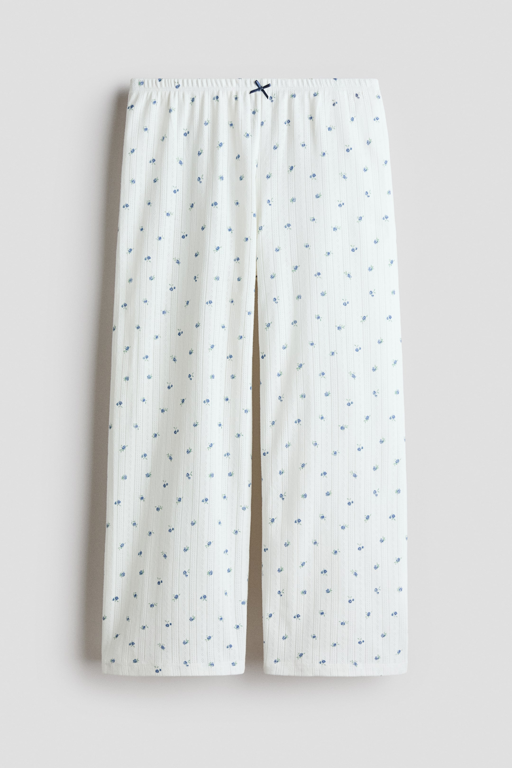 View larger image: Pyjama bottoms are shown in a front view, crafted from white pointelle jersey adorned with a scattered blue floral pattern. They boast a narrow elasticated waist, accented by a small dark blue satin bow at the front, and feature straight legs.