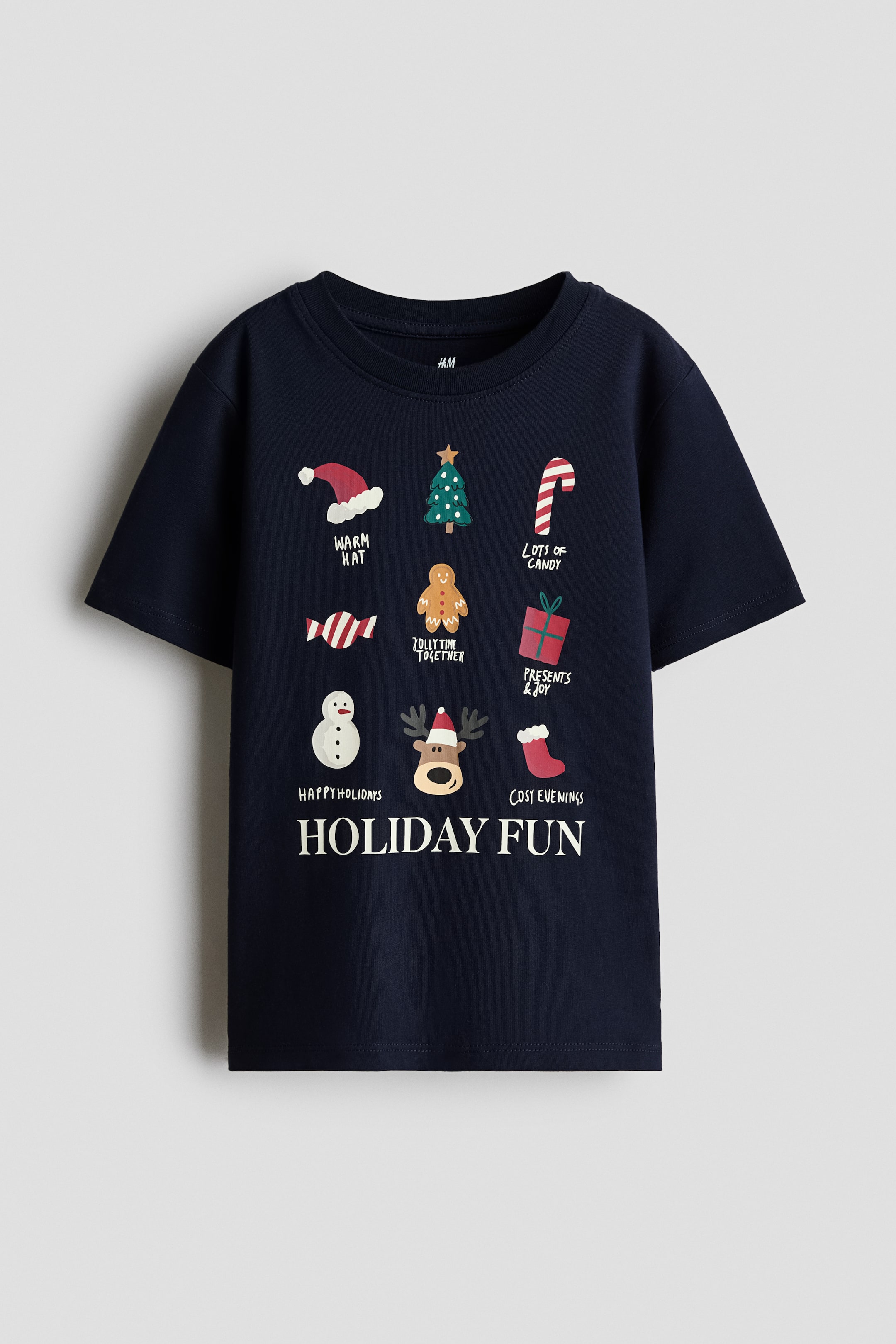 View larger image: A navy blue T-shirt is shown from the front, featuring a crew neck and short sleeves. The front displays a grid of festive holiday-themed illustrations with small text captions, including a Santa hat, Christmas tree, candy cane, gingerbread man, gift box, snowman, reindeer, and stocking, above the bold white text "HOLIDAY FUN".