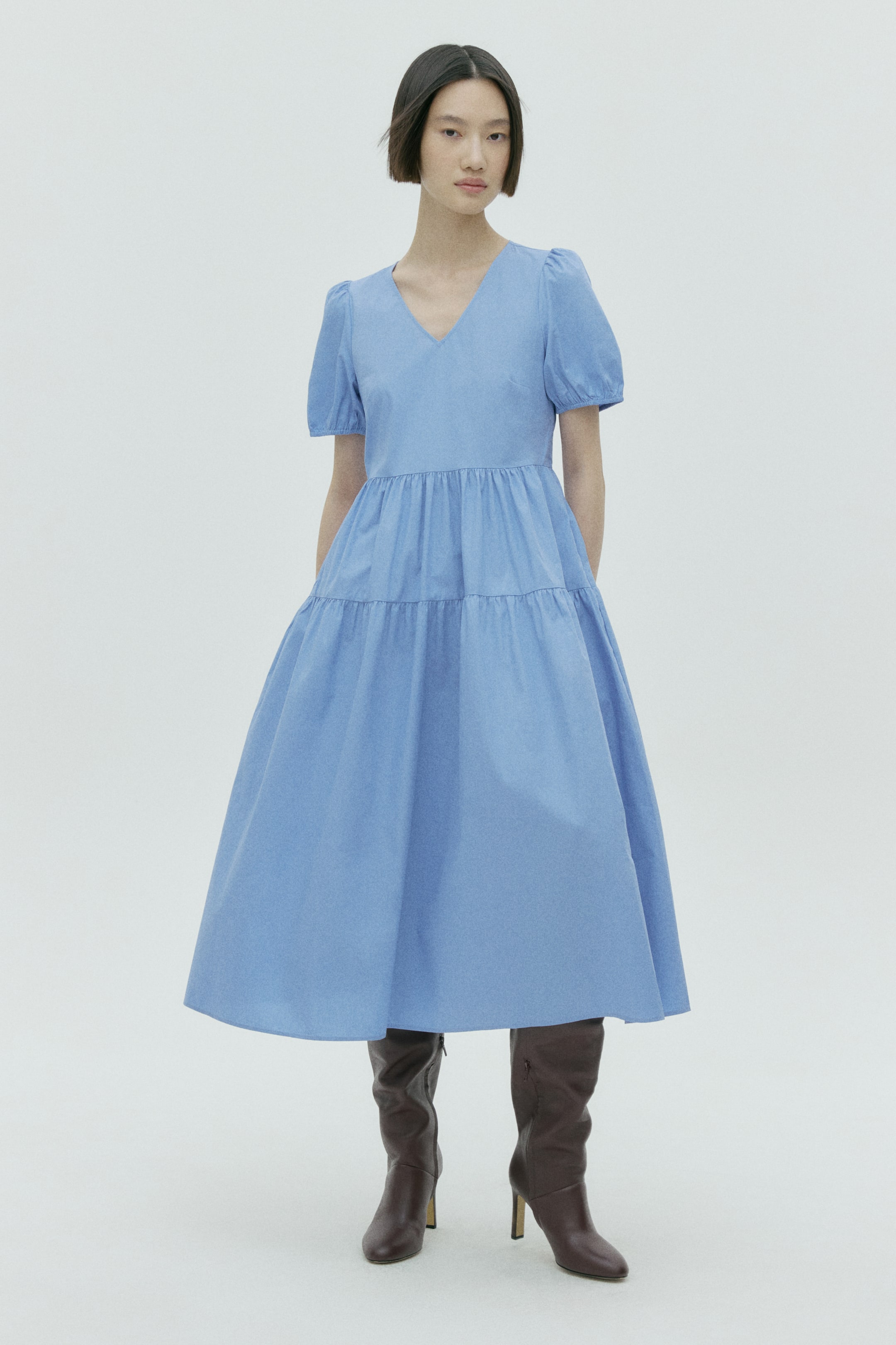 View larger image: A light blue calf-length dress features a V-neckline and short puffed sleeves. It showcases a fitted bodice and a tiered, gathered skirt, creating a full, flowing silhouette.