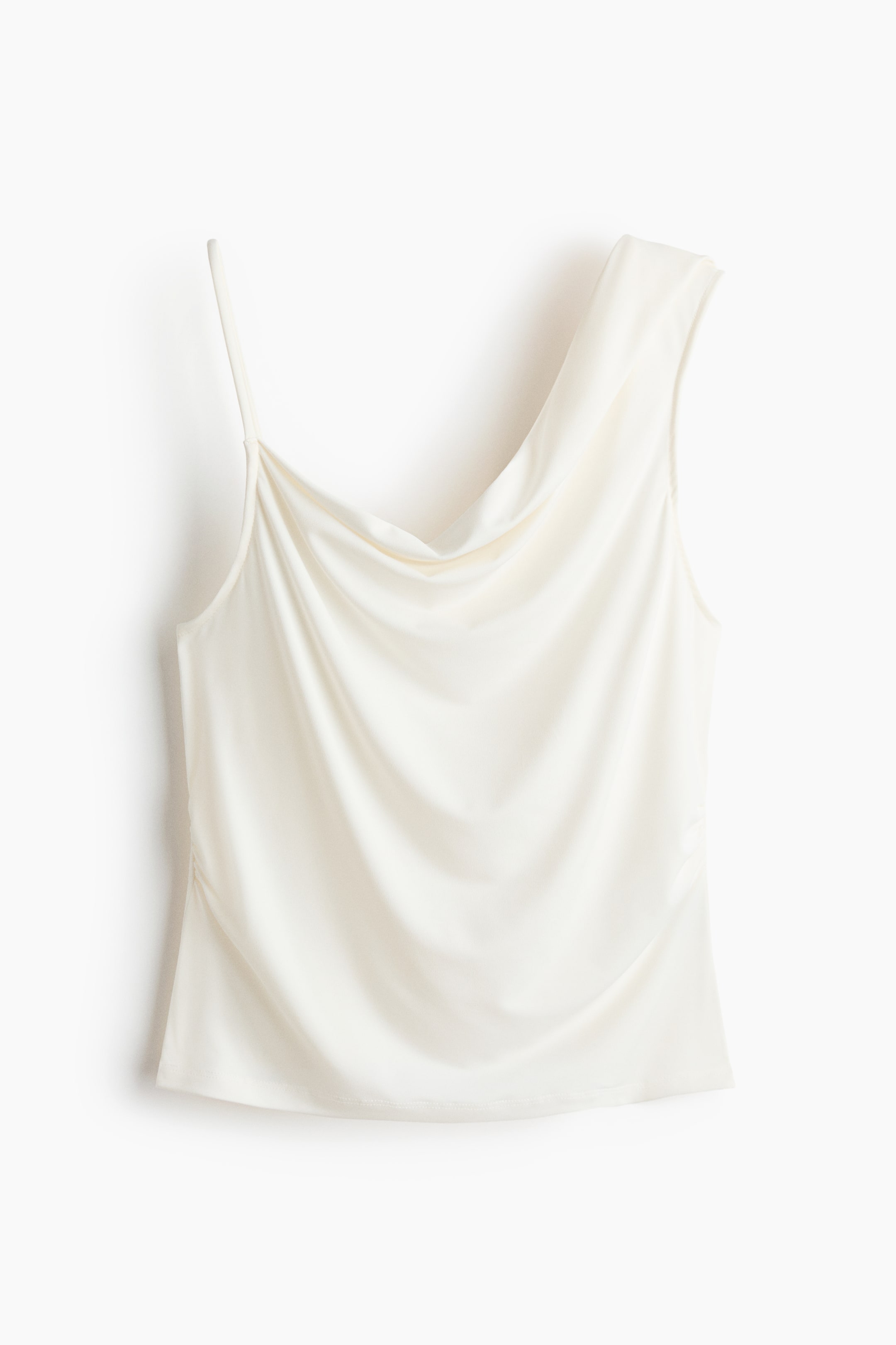 View larger image: An off-white asymmetrical cowl neck top features a thin spaghetti strap on the left shoulder and a broader, draped shoulder on the right. The fabric gently cascades across the chest, with ruching forming along the left side seam.