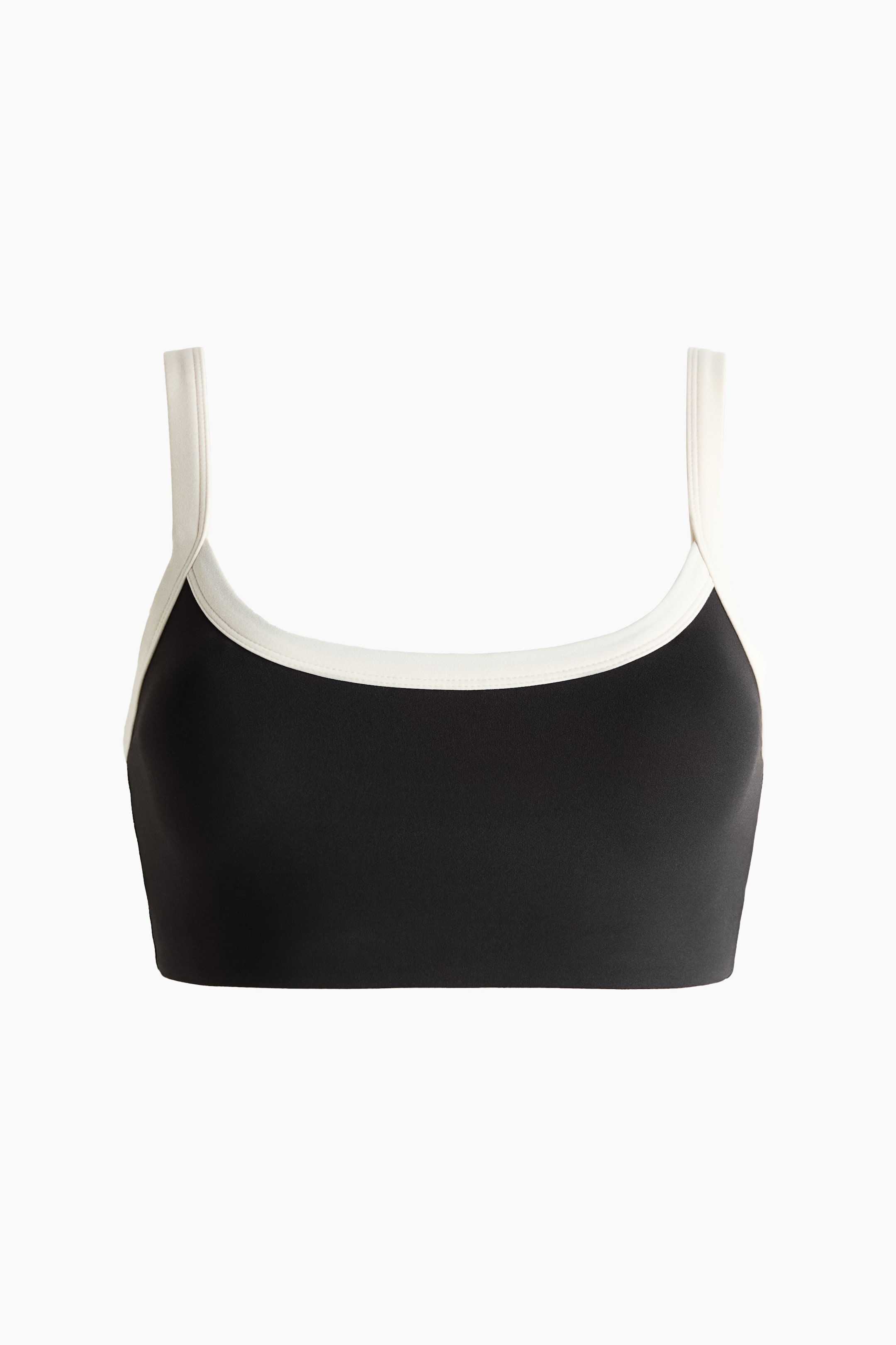 Ver imagem maior: Um soutien desportivo cropped preto, visto de frente, apresenta um decote redondo e alças largas em tom branco-creme contrastante.