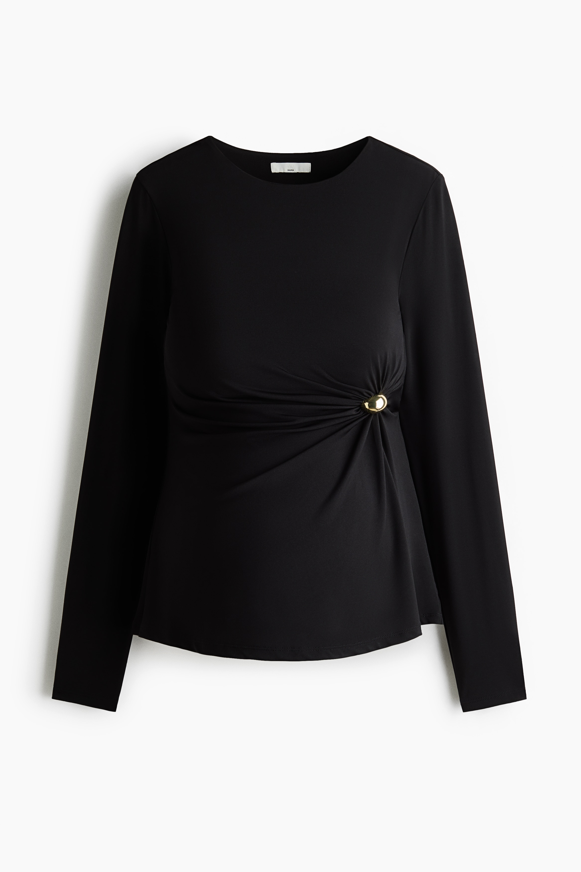 The model is wearing a fitted black jersey top with a round neckline and long sleeves, featuring a circular metal detail on one side that gathers the fabric to create a draped effect. The top is styled with light-coloured, wide-leg trousers.