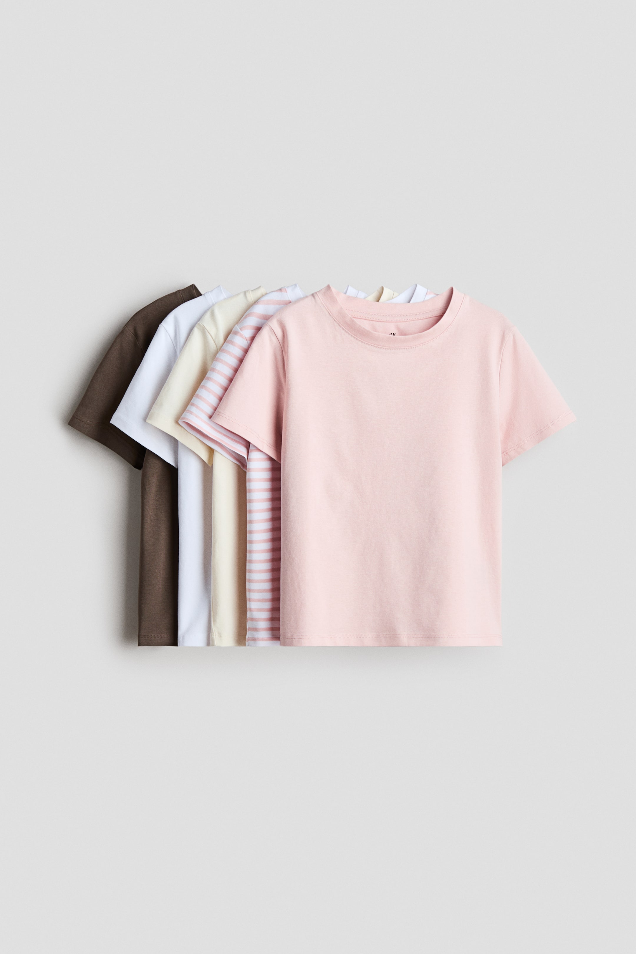 Agrandir l'image: Des t-shirts en jersey de coton doux avec une bordure côtelée autour de l'encolure et des épaules légèrement tombantes sont présentés. Le t-shirt le plus en avant est rose clair, avec d'autres t-shirts à rayures, crème, blanc et marron superposés derrière lui.