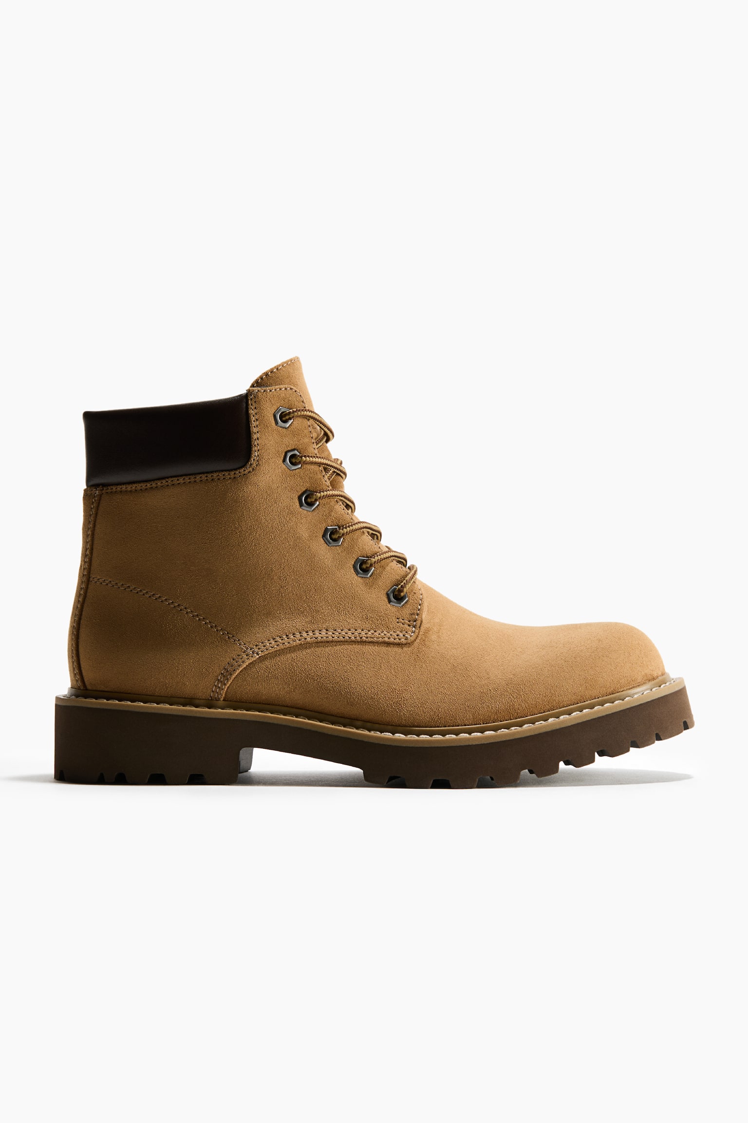 Une botte lacÃ©e en suÃ©dine beige est prÃ©sentÃ©e en vue de profil, avec un col de cheville rembourrÃ© marron foncÃ© et des Åillets mÃ©talliques assortis Ã  des lacets beiges. La botte repose sur une semelle crantÃ©e Ã©paisse marron foncÃ©, avec une couture crÃ¨me visible le long du montage.