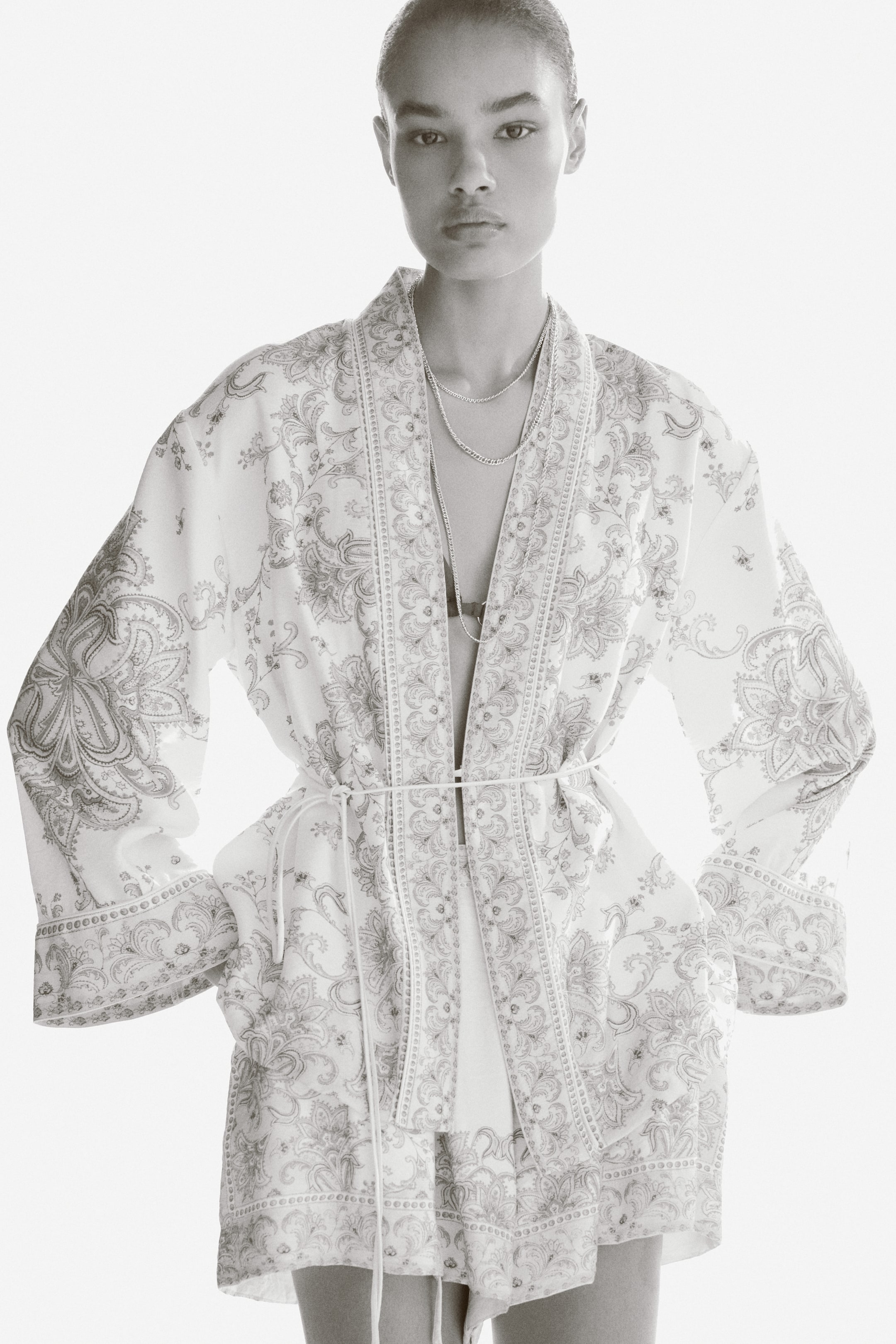 View larger image: The model is showcasing a viscose-blend blazer adorned with an all-over print and accented by narrow piping. This blazer boasts a wrapover front, dropped shoulders, and long, wide sleeves. It is elegantly cinched at the waist with a spaghetti tie belt, worn over a coordinating top and matching shorts.
