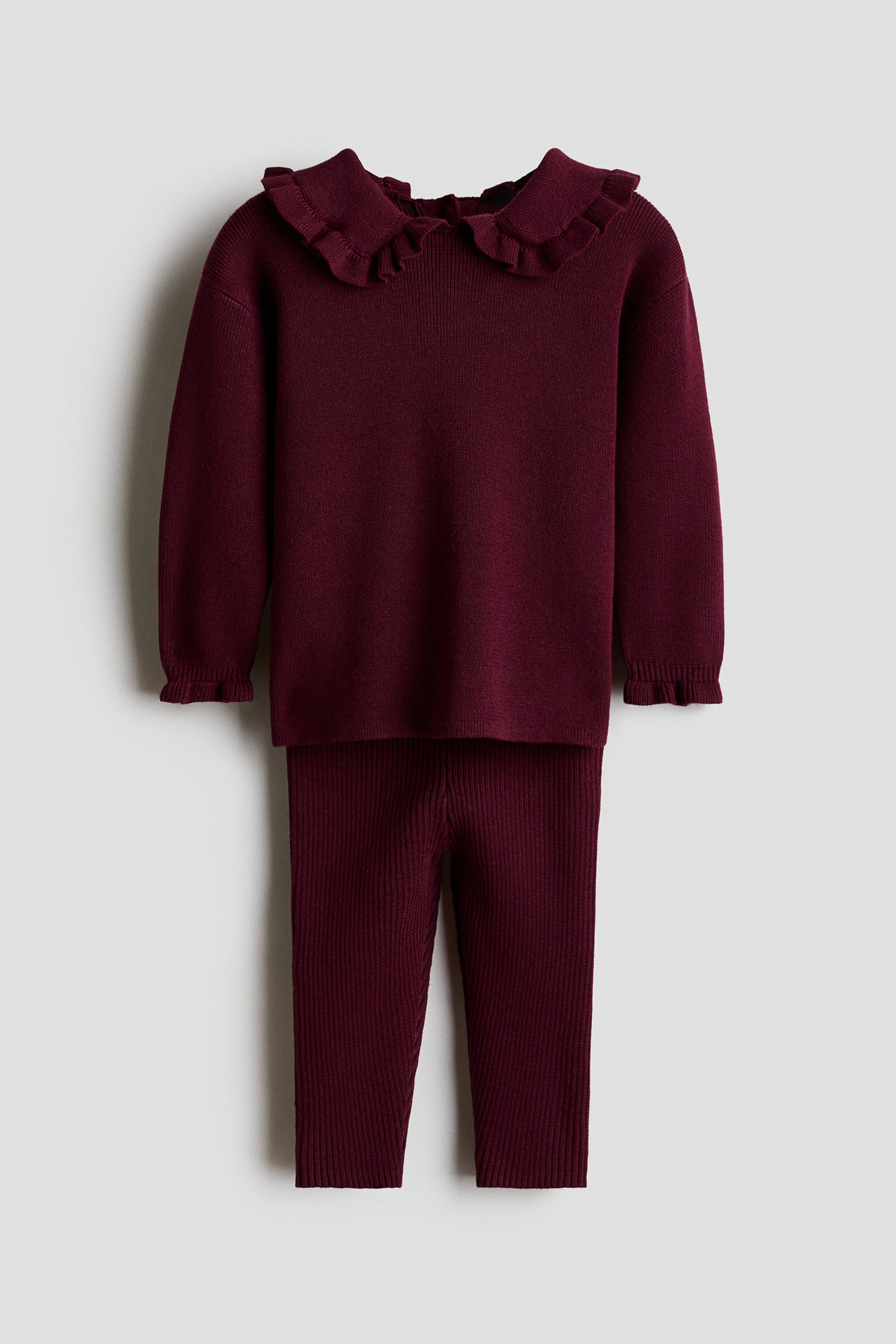 View larger image: An H&M Adorables set showcases a long-sleeved dark red jumper and matching ribbed leggings, presented front-facing. The jumper features a frill-trimmed collar, dropped shoulders, and frilled cuffs.
