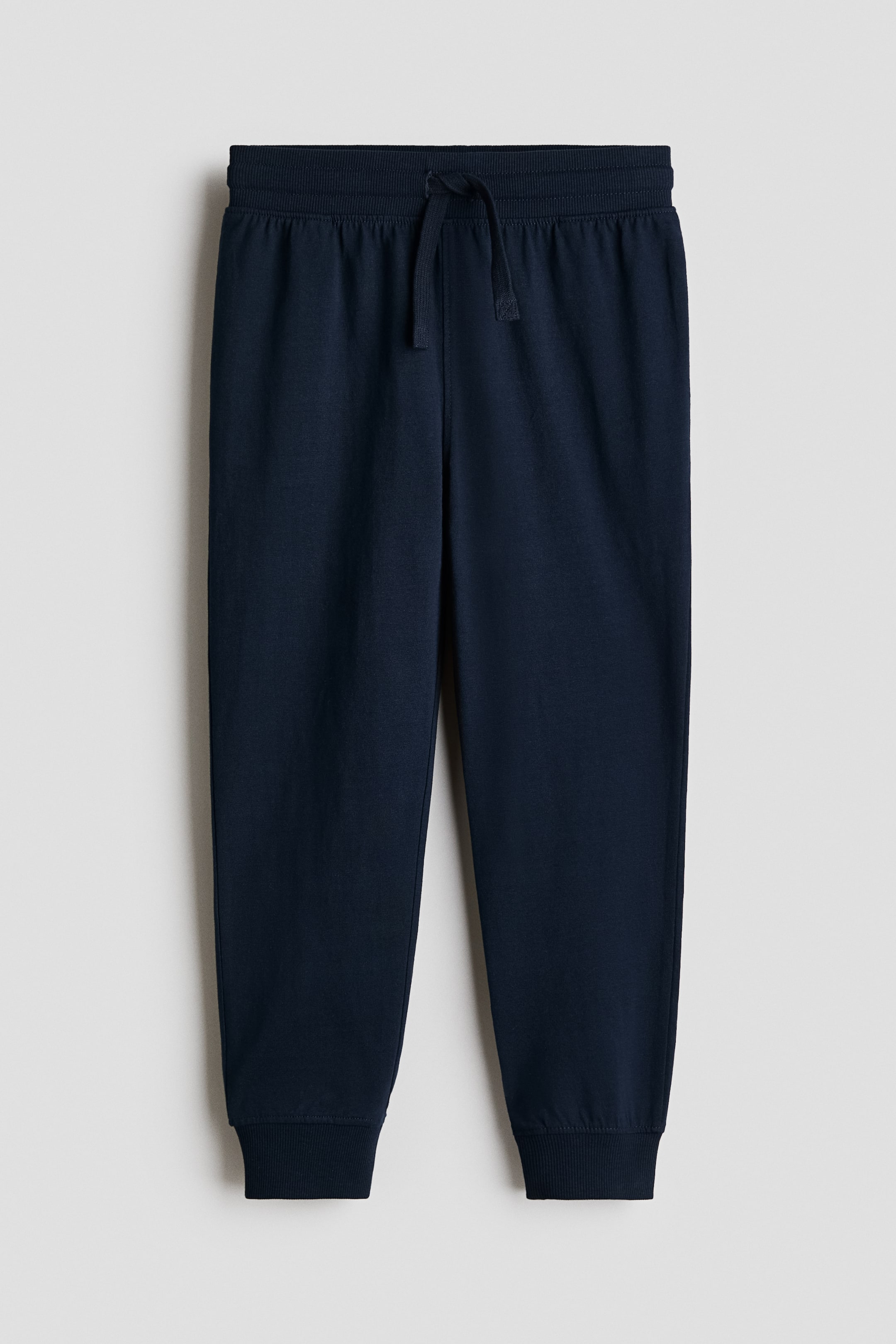 View larger image: Navy blue joggers featuring an elasticated drawstring waist with the drawstring tied in a bow, a soft cotton jersey construction, and ribbed cuffs at the hems.