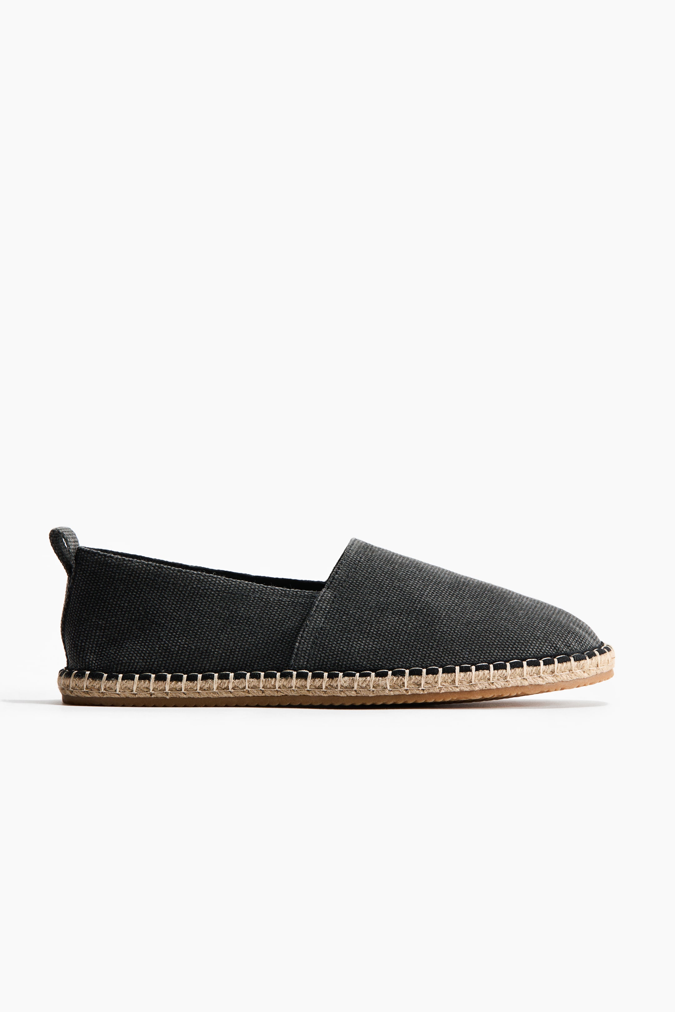 View larger image: A dark grey canvas espadrille shoe is showcasing its side profile. It features a jute-wrapped sole with prominent white stitching connecting the upper, and a fabric pull tab extends from the heel.