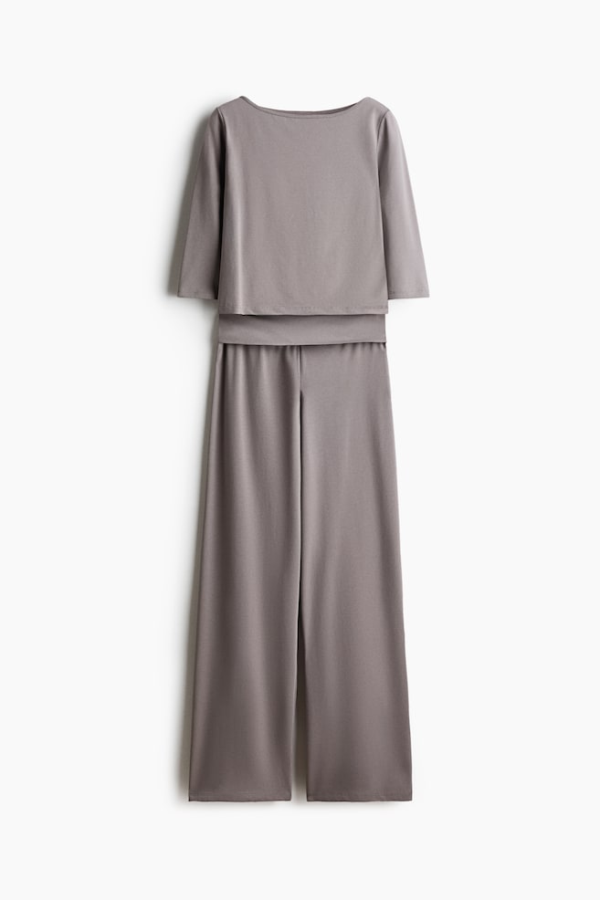 A taupe-grey two-piece set is displayed in a front-facing view, featuring a boat-neck top with three-quarter-length sleeves and a layered hem, paired with matching high-waisted wide-leg trousers. - 1