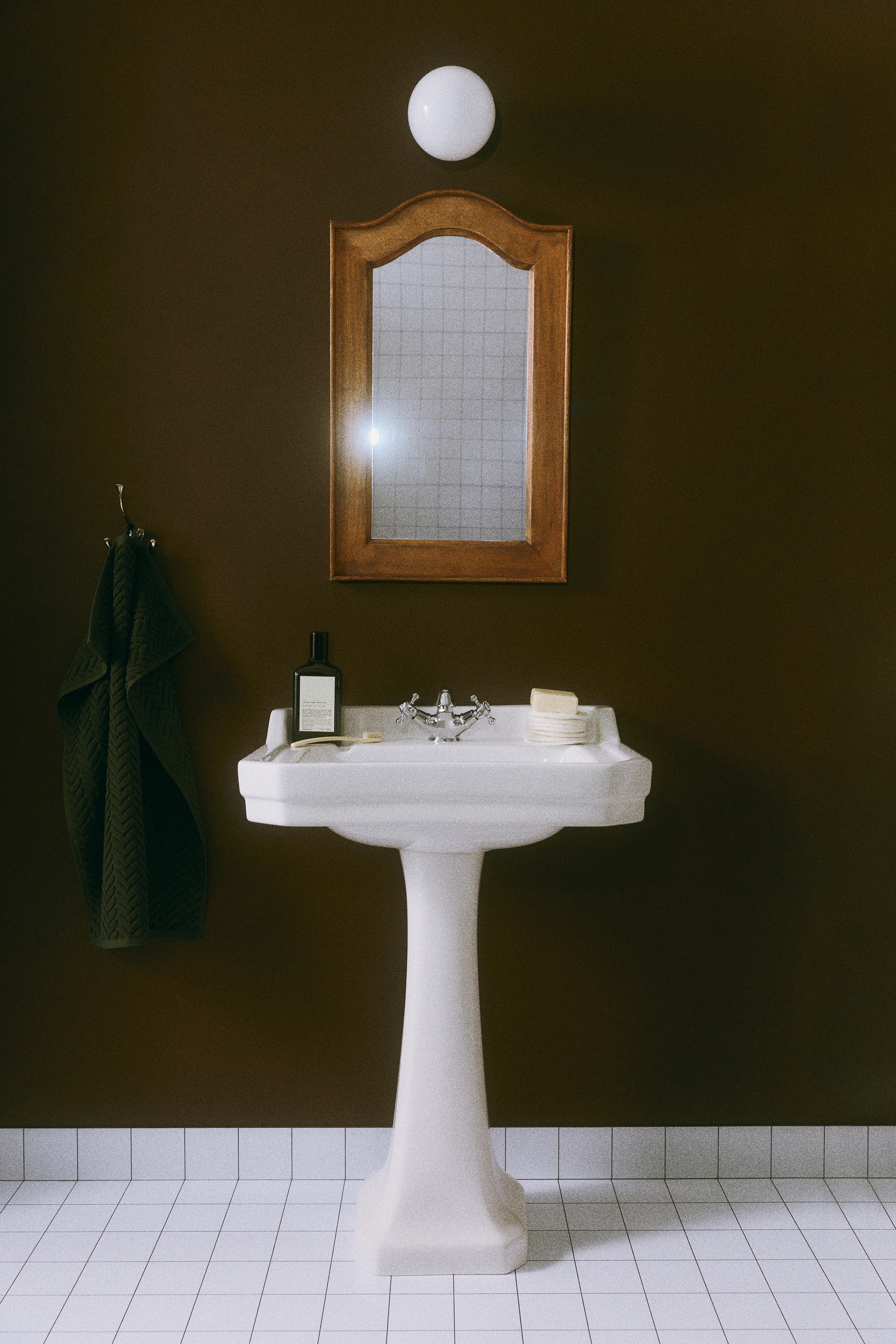 A dark green terry cloth hand towel is hanging vertically from a small black peg, displaying a textured chevron pattern resembling a cable-knit design. The top corner is folded over to show the reverse side of the textured fabric and its finished hem.